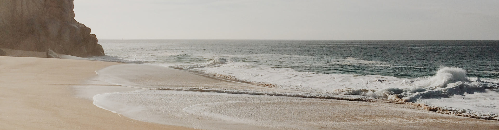 A SAND BEACH WITH WAVES FROM THE OCEAN CRASHING ONTO THE SHORE