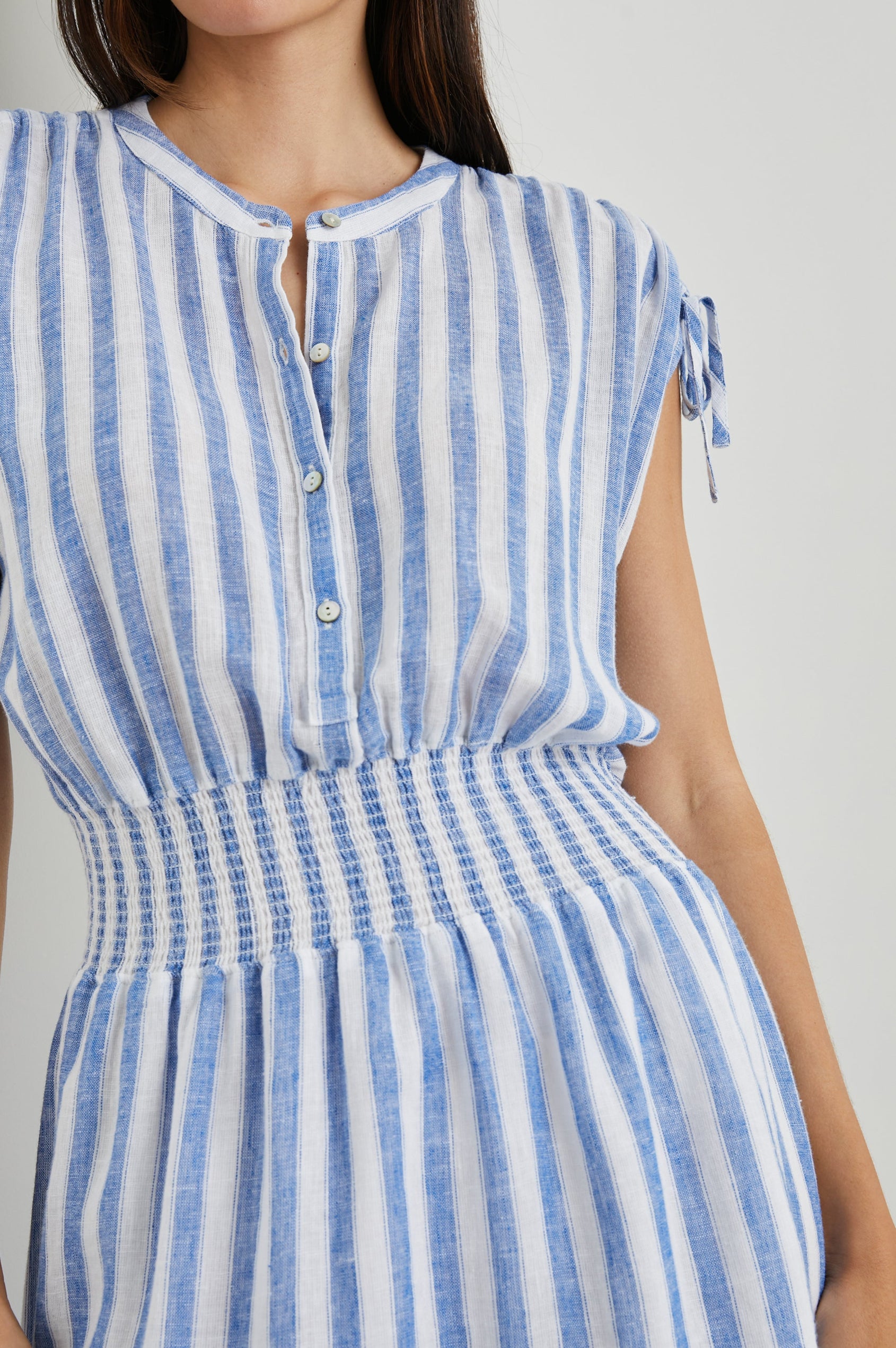 Samina Above-Knee Sleeveless Dress with drawstrings at the Sleeve Openings, Buttons along the Bodice, A Cinched Waist and a Tiered Skirt in Casablanca Stripe Colorway, with blue vertical stripes on white - Front View Featured on Model