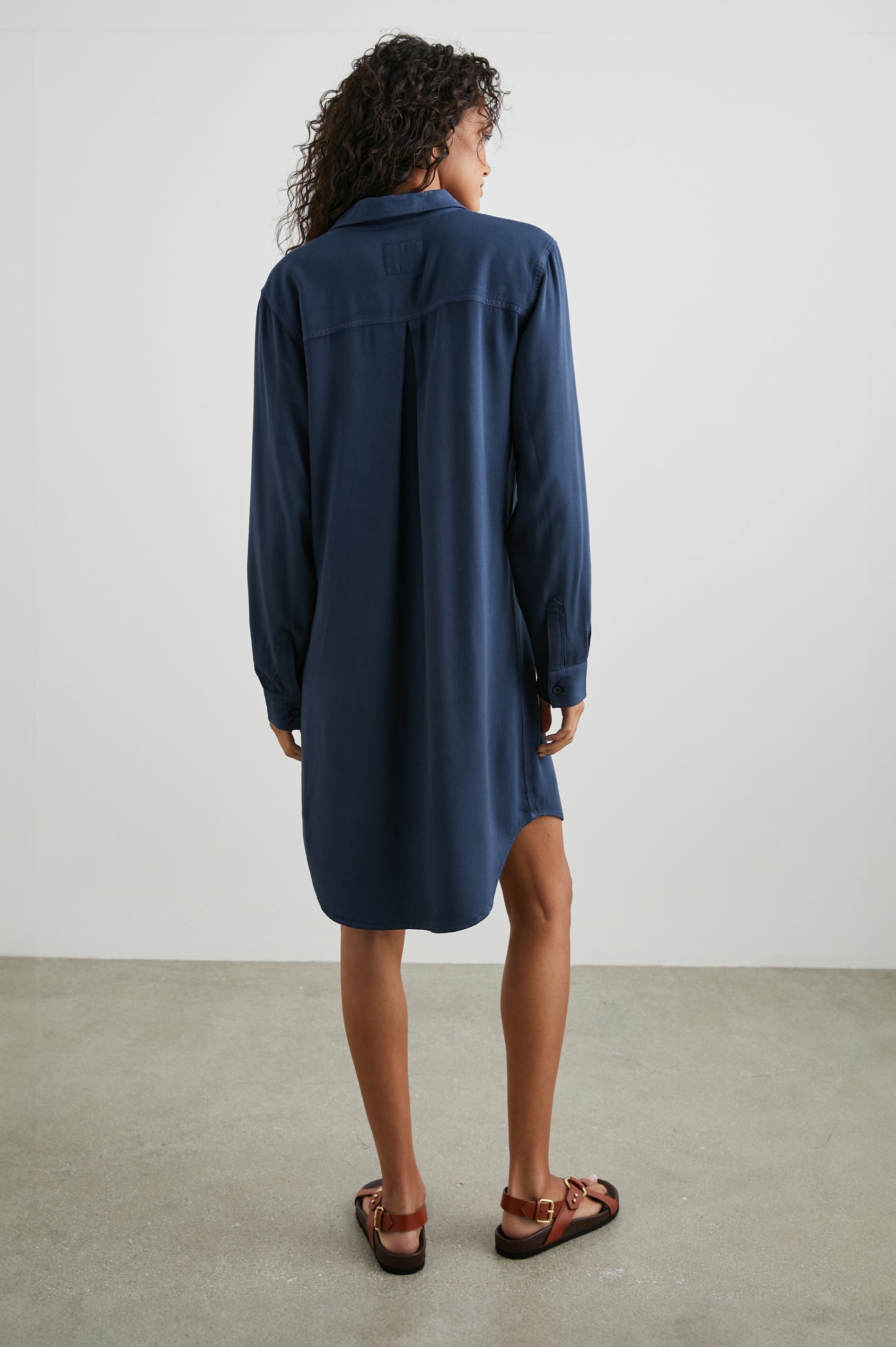 Sawyer Long-Sleeve Mini Dress with a Full Button Front, a Chest Patch Pocket, a Collar, Button Cuffs and a Low High Hem in Navy Colorway - Back Full Body View Featured on Model