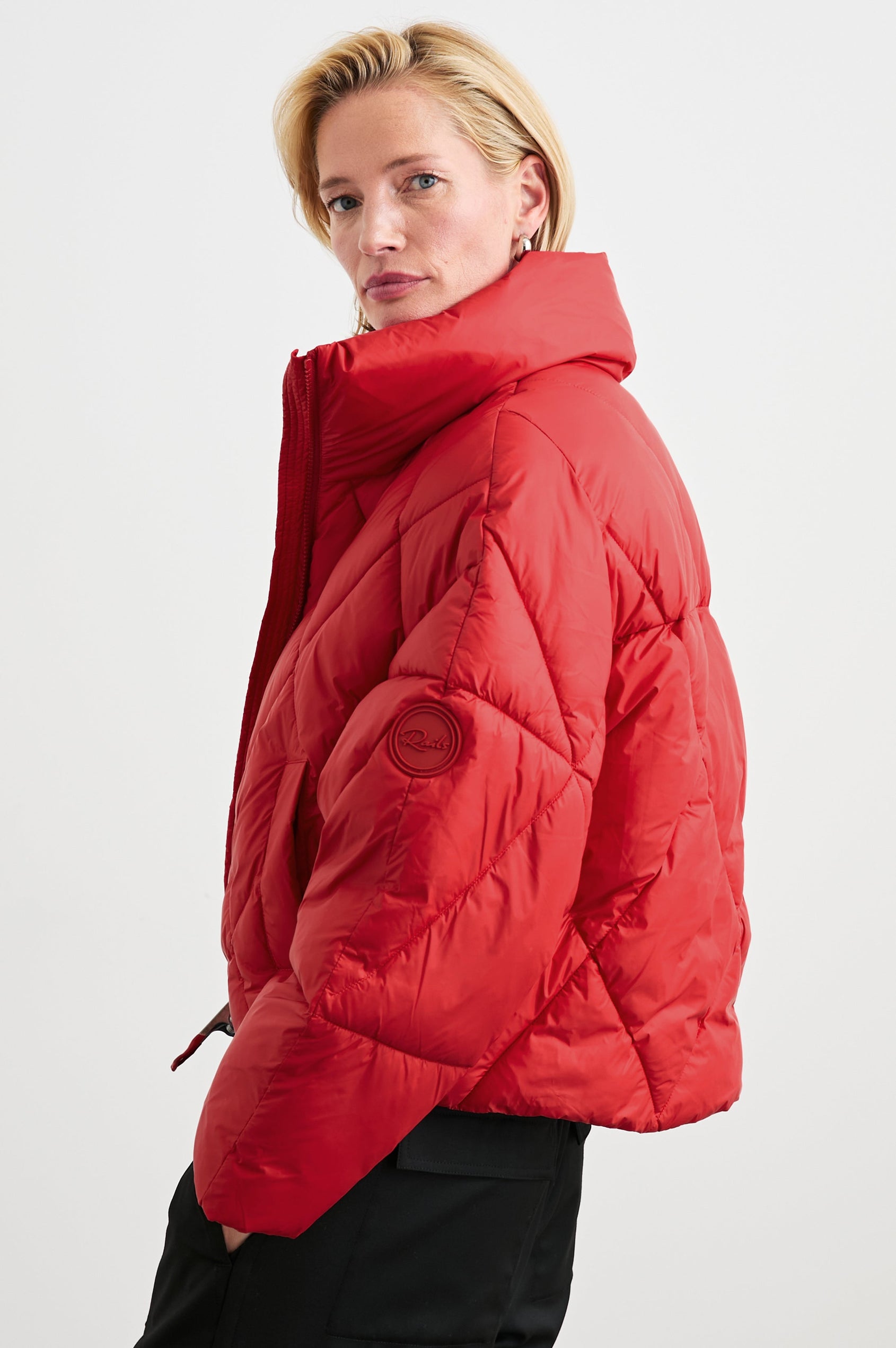 Summit Cropped Puffer Jacket with a Mid-Neck Collar, Two Pockets and a Rails Logo on the Arm in Scarlet Colorway - Side View Featured on Model