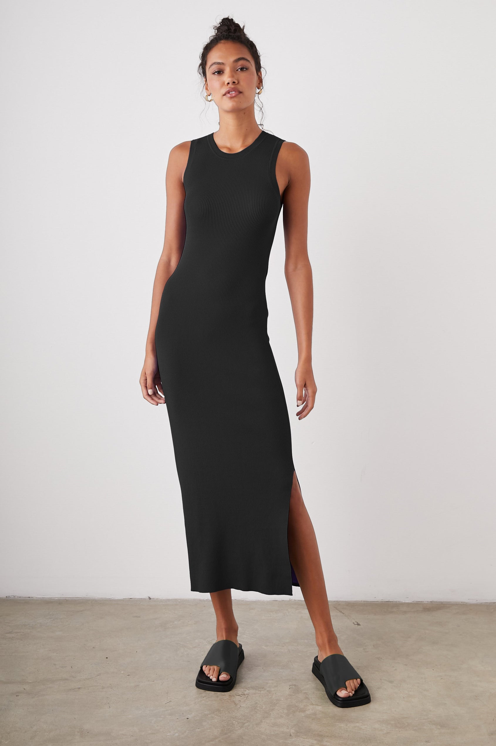 Syd Ribbed, Sleeveless Midi Dress with Wide Shoulder Straps, a Side Slit, and a Cutout that Spans the Lower Back in Black Colorway - Front Full Body View Featured on Model