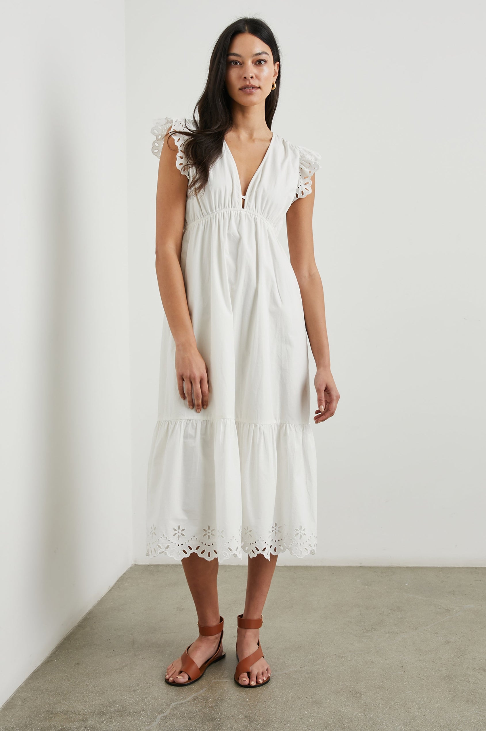 Tina Short Sleeve Midi Dress with Flutter Sleeves, a Deep V Neck with a Cutout and a Tiered Skirt in White Colorway, with eyelets on the Sleeves and an Eyelet Floral Pattern on the Hem - Front Full Body View Featured on Model