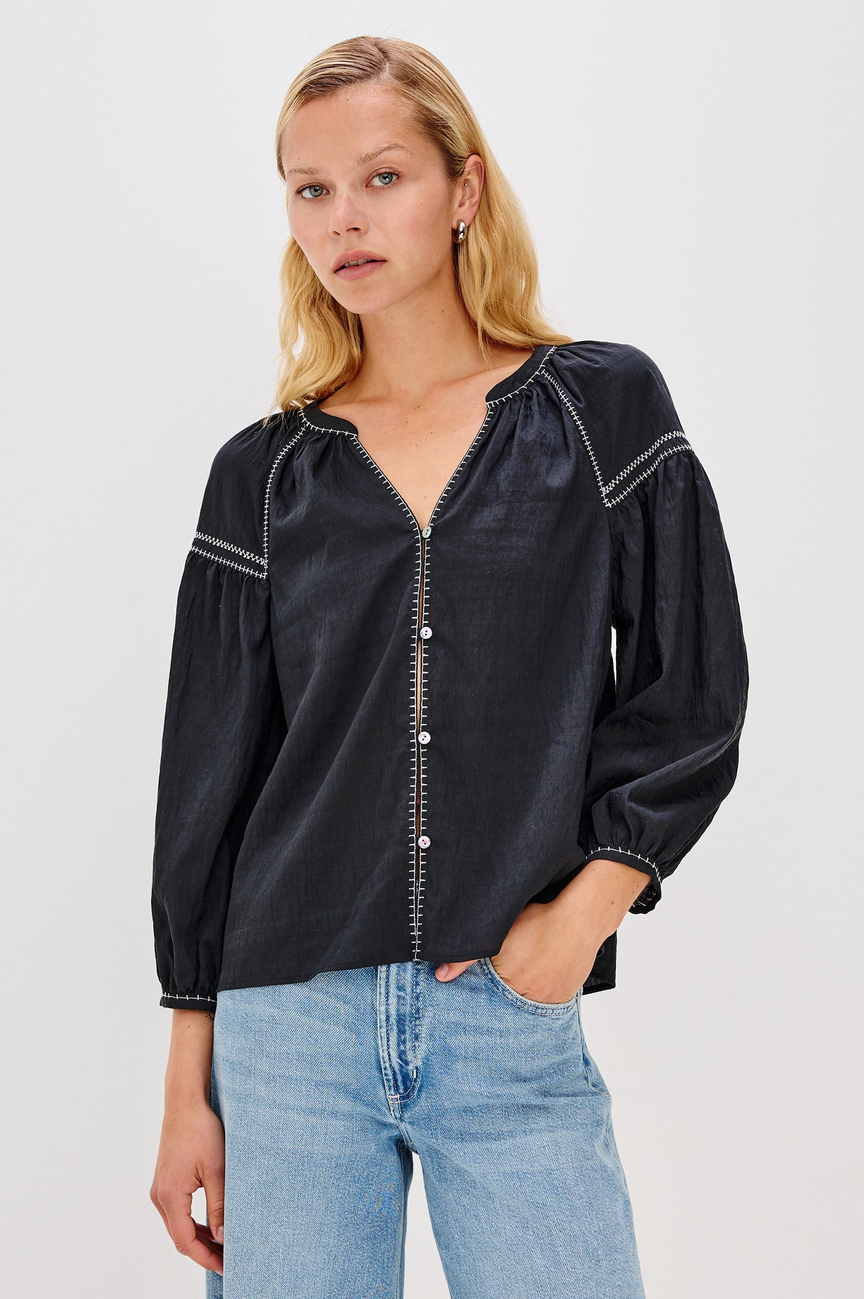 The Vasia is a long sleeve peasant top with a v-neck and button front, contrast white stitching and elastic at sleeve hems in Black colorway. Front view featured on model.