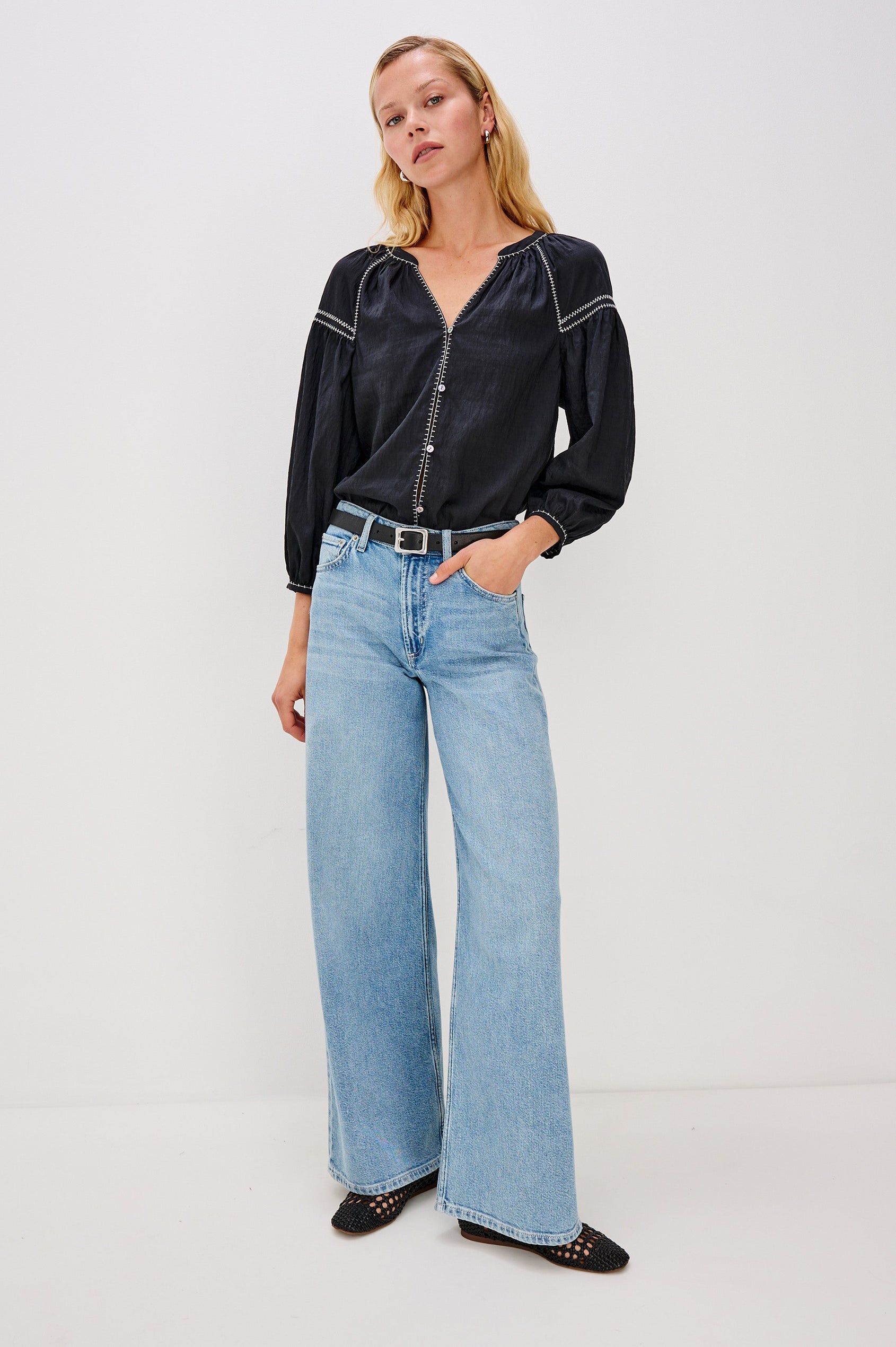 The Vasia is a long sleeve peasant top with a v-neck and button front, contrast white stitching and elastic at sleeve hems in Black colorway. Front full body view featured on model.