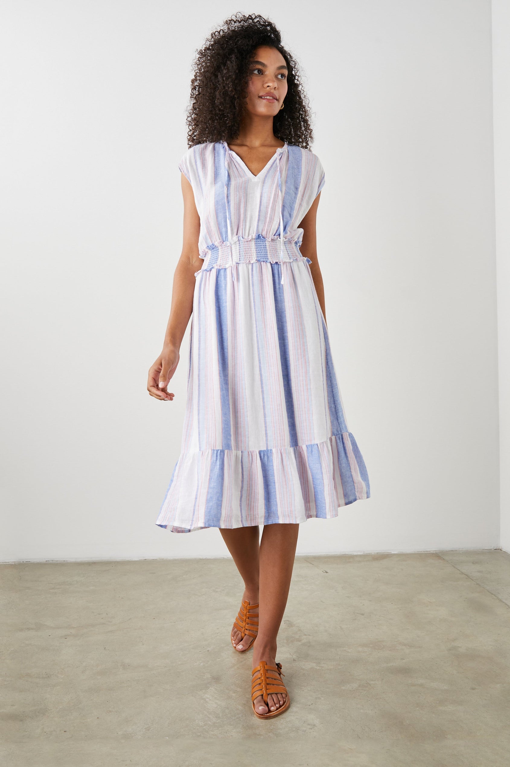 Ashlyn Short Sleeve Midi Dress with a V neck with Ties, a Smocked Waist and a Ruffle Tier at the Hem in Marini Stripe Colorway, Vertical Stripes in Pink and Blue on White - Front Full Body View Featured on Model