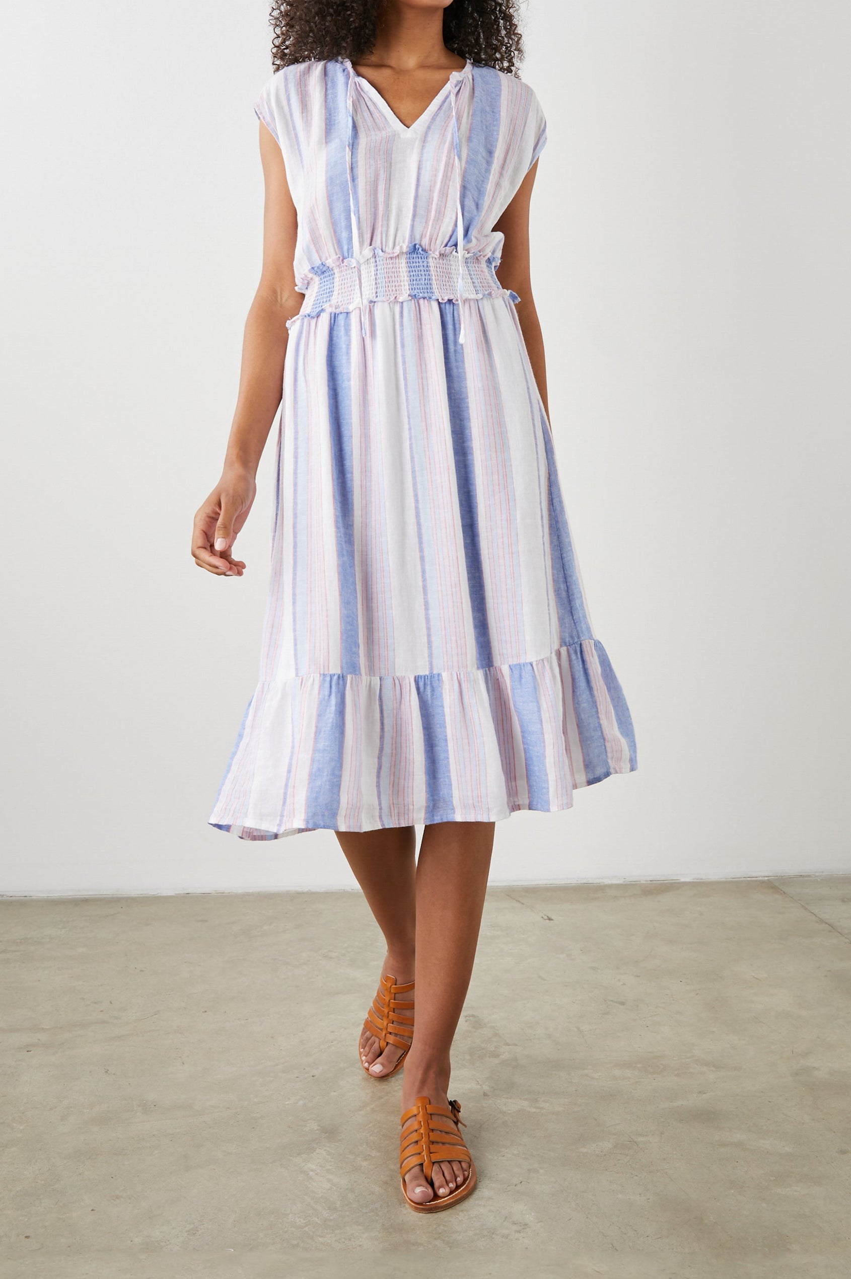 Ashlyn Short Sleeve Midi Dress with a V neck with Ties, a Smocked Waist and a Ruffle Tier at the Hem in Marini Stripe Colorway, Vertical Stripes in Pink and Blue on White - Front Full Body View Featured on Model