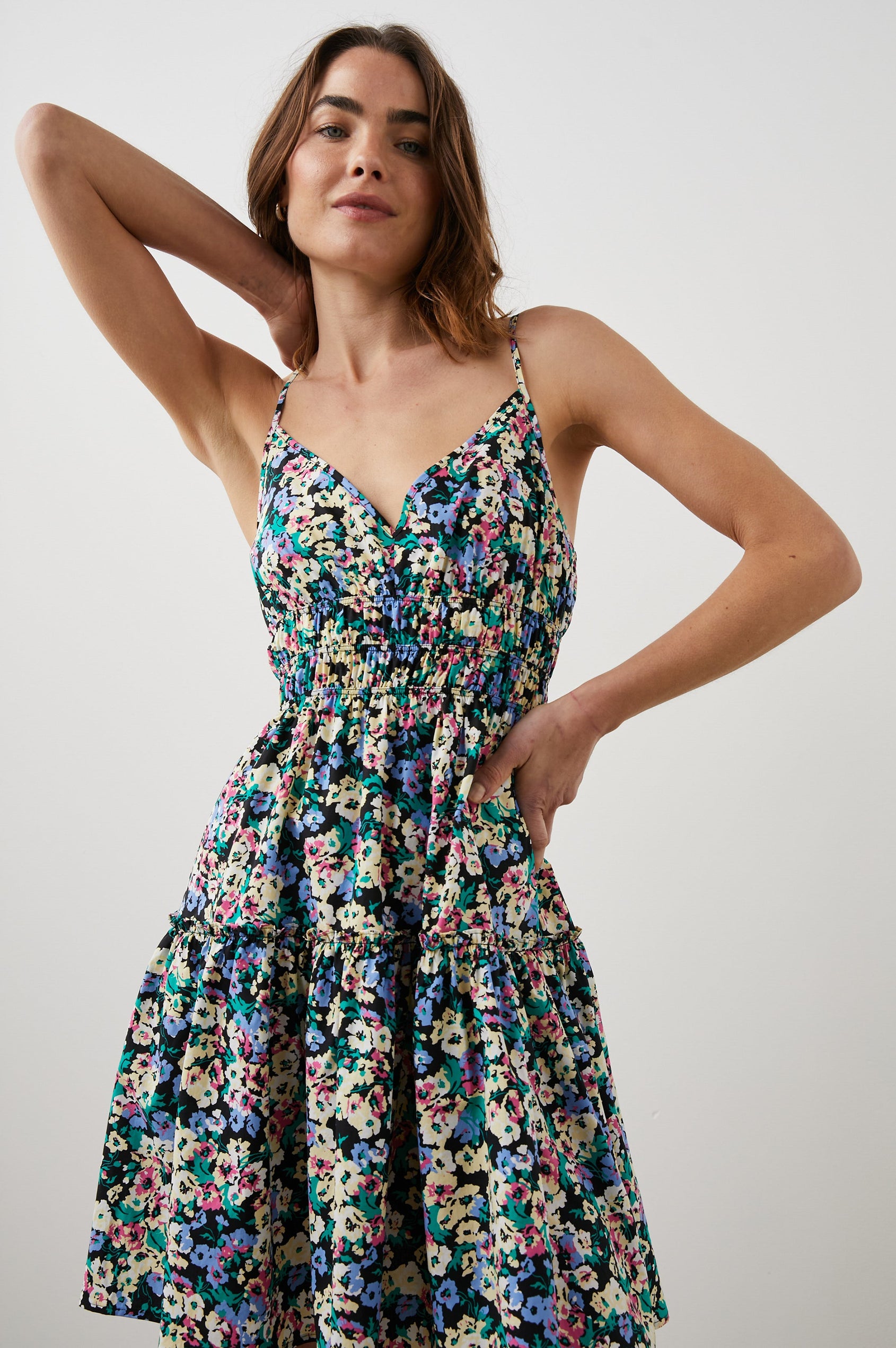 Carmen Sleeveless Mini Dress with Adjustable Spaghetti Straps, a Deep V Neck, a Tiered Skirt and Smocking at the Mid-Bodice in Wildflower Meadow Colorway, Yellow, Purple, Green and Pink on Black - Front View Featured on Model