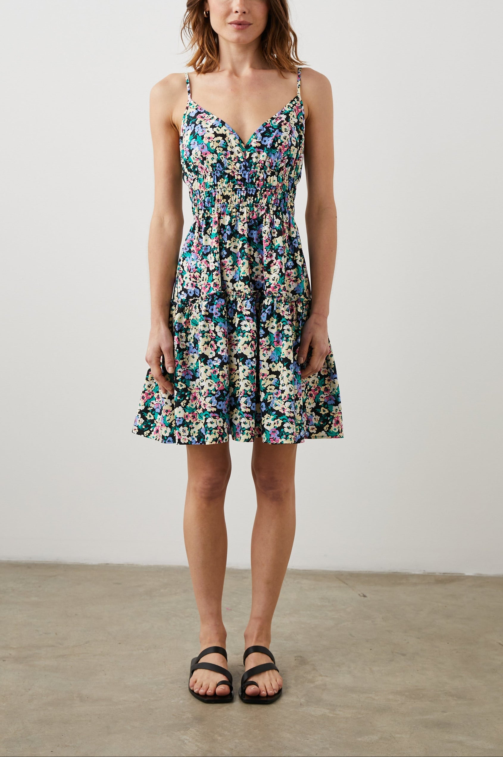 Carmen Sleeveless Mini Dress with Adjustable Spaghetti Straps, a Deep V Neck, a Tiered Skirt and Smocking at the Mid-Bodice in Wildflower Meadow Colorway, Yellow, Purple, Green and Pink on Black - Front Full Body View Featured on Model