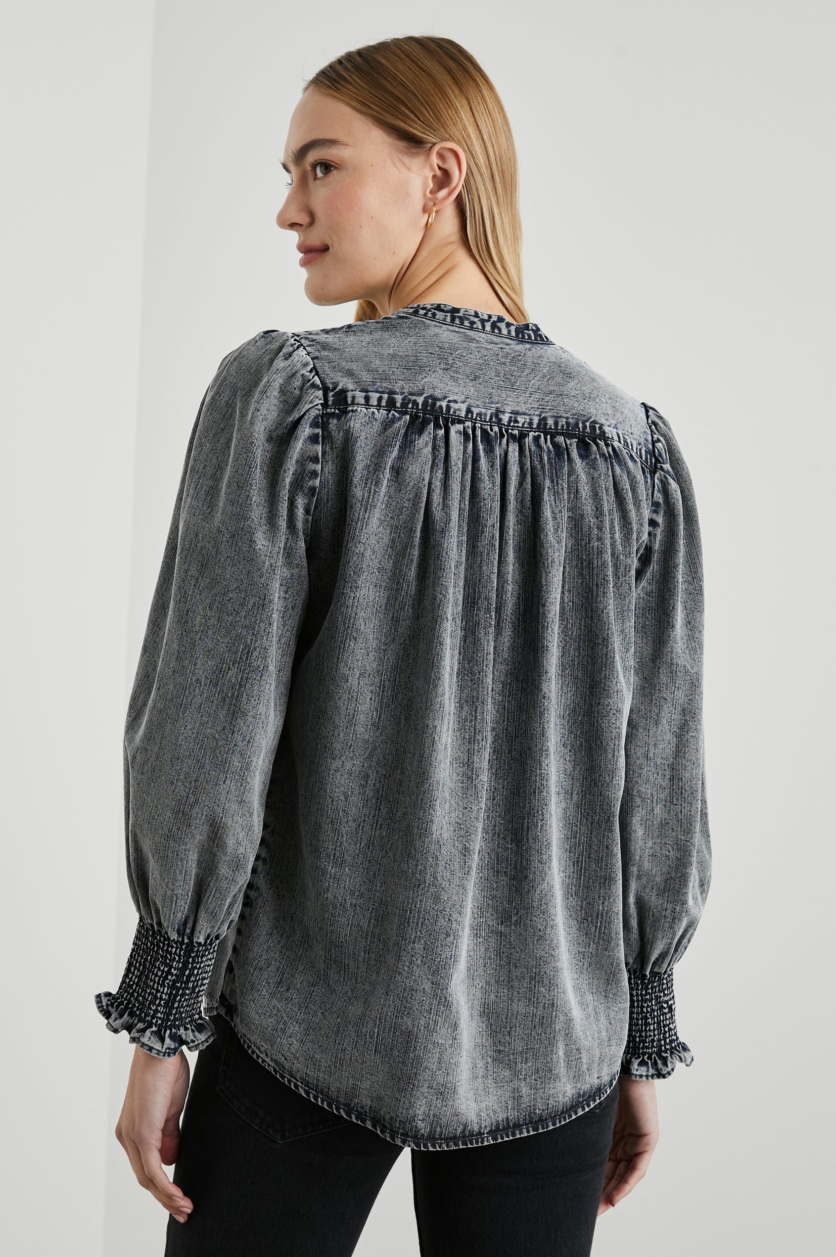 Daphne Long Sleeve Denim Shirt with Front Button Closure, Shirred and Ruffled Cuffs, and Ruching along the Yoke Seams in Ink Wash Colorway - Back View Featured on Model