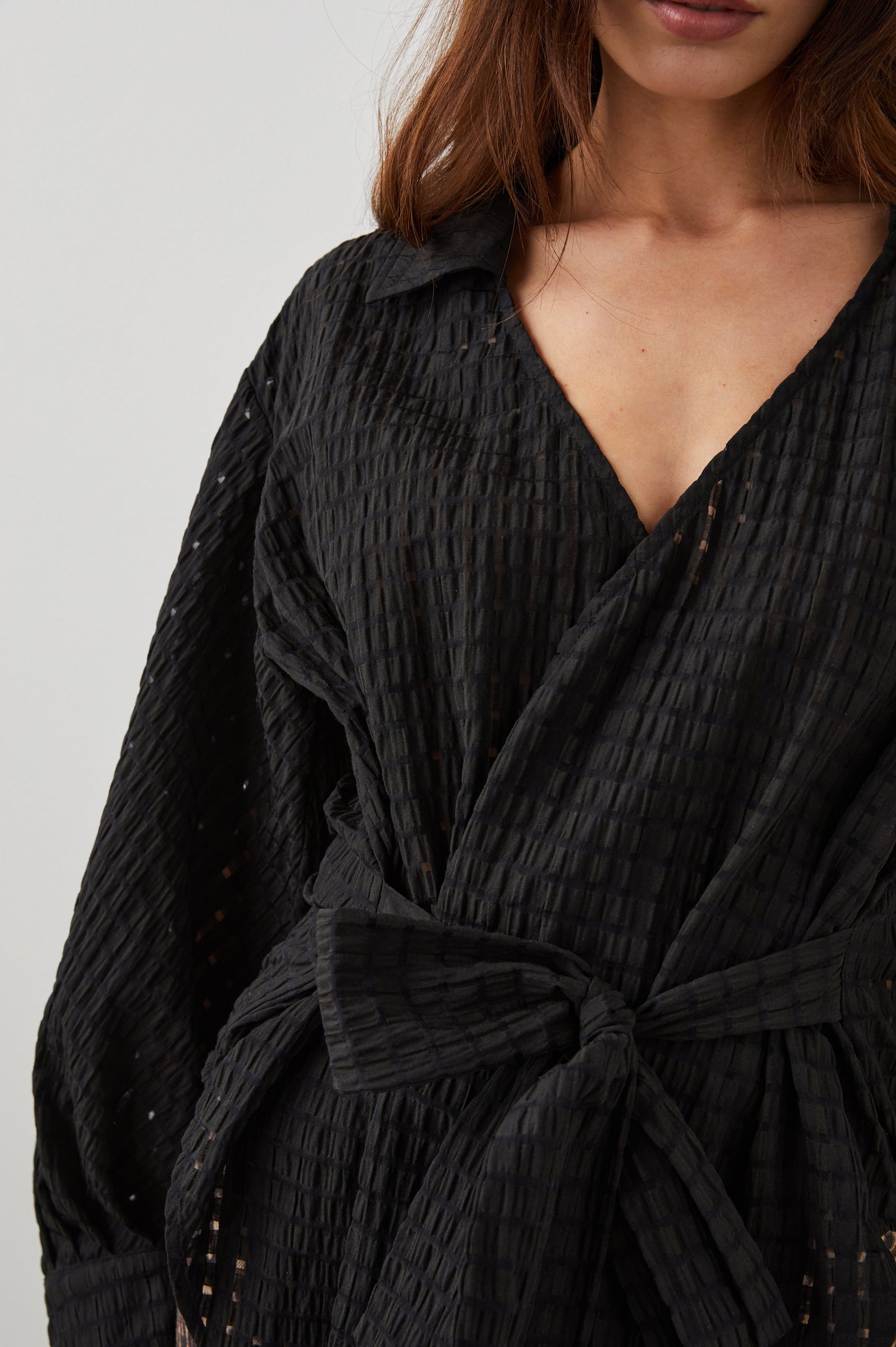 Eileen Long-Sleeve Wrap Top with Textured Fabric, a Deep V Neck, a Collar, a Wrap Tie at the Waist, Billowy Sleeves, in Black Seersucker Colorway - Front View Featured on Model