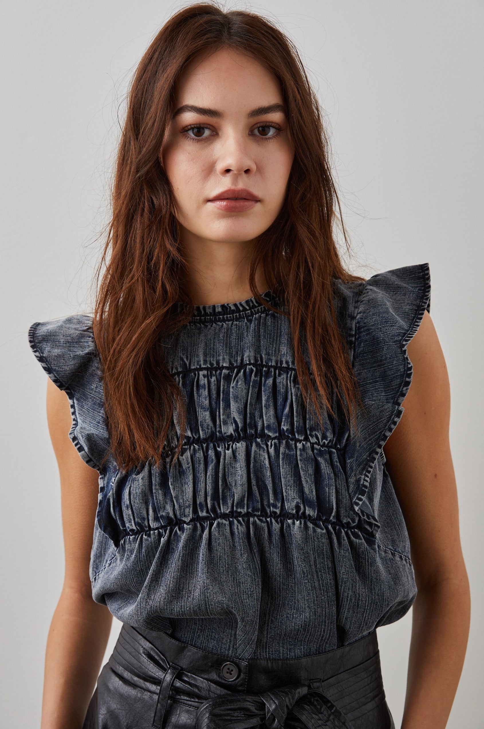 Filomena Short Sleeve Denim Top with Flutter Sleeves, a Ruffled Neck, a Shirred Center Bodice, Lace Inserts and a Buttoned Keyhole at the Back in Ink Wash Colorway - Front Tucked View Featured on Model