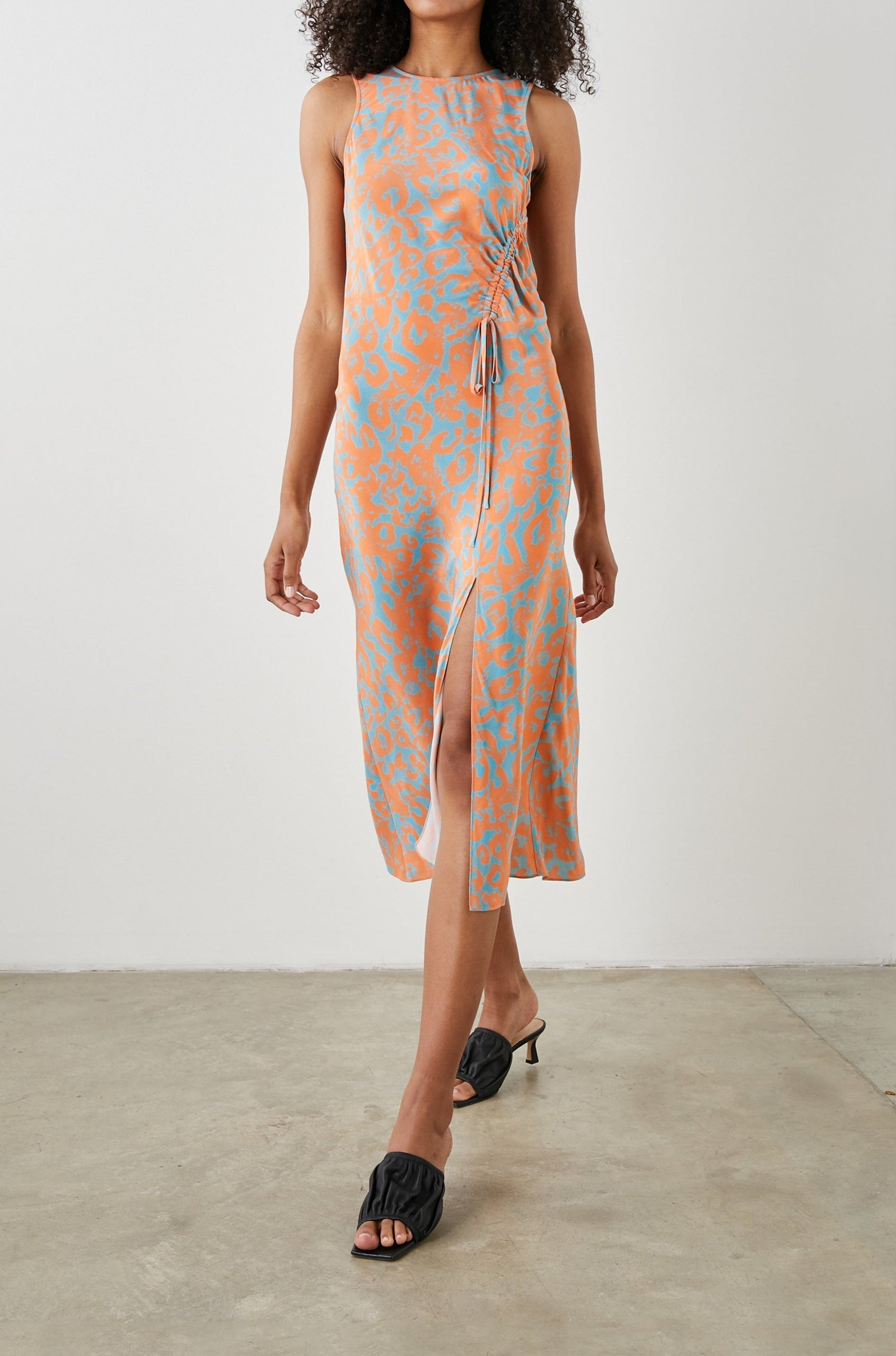 Gabriella Sleeveless Midi Dress with a Crew Neck, a Left Thigh Side Slit, a Ruched Drawstring on the Left Side and a Keyhole Button Closure at the Back in Orange Diffused Cheetah Colorway, Orange Spots on Blue - Front Full Body View Featured on Model