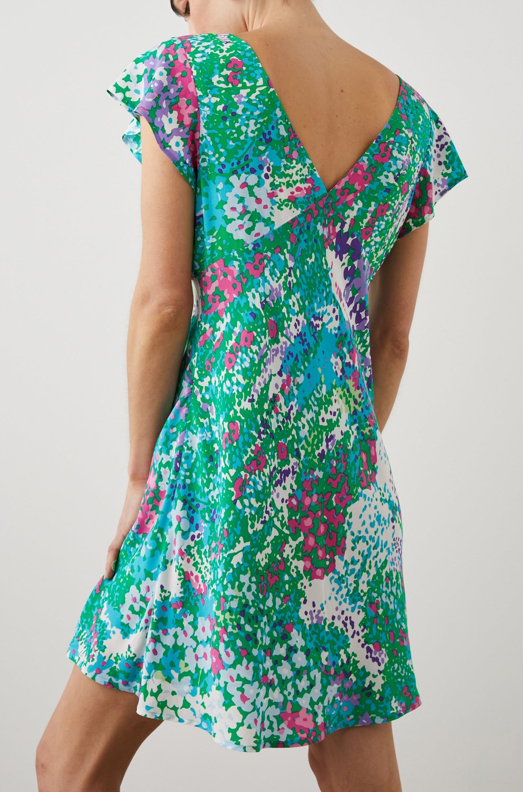 Gigi Short Sleeve Mini Dress with a Deep V Neck, and Flutter Sleeves in Gardenia Floral Colorway, Greens, Blues, Purples, Pink and White - Back View Featured on Model