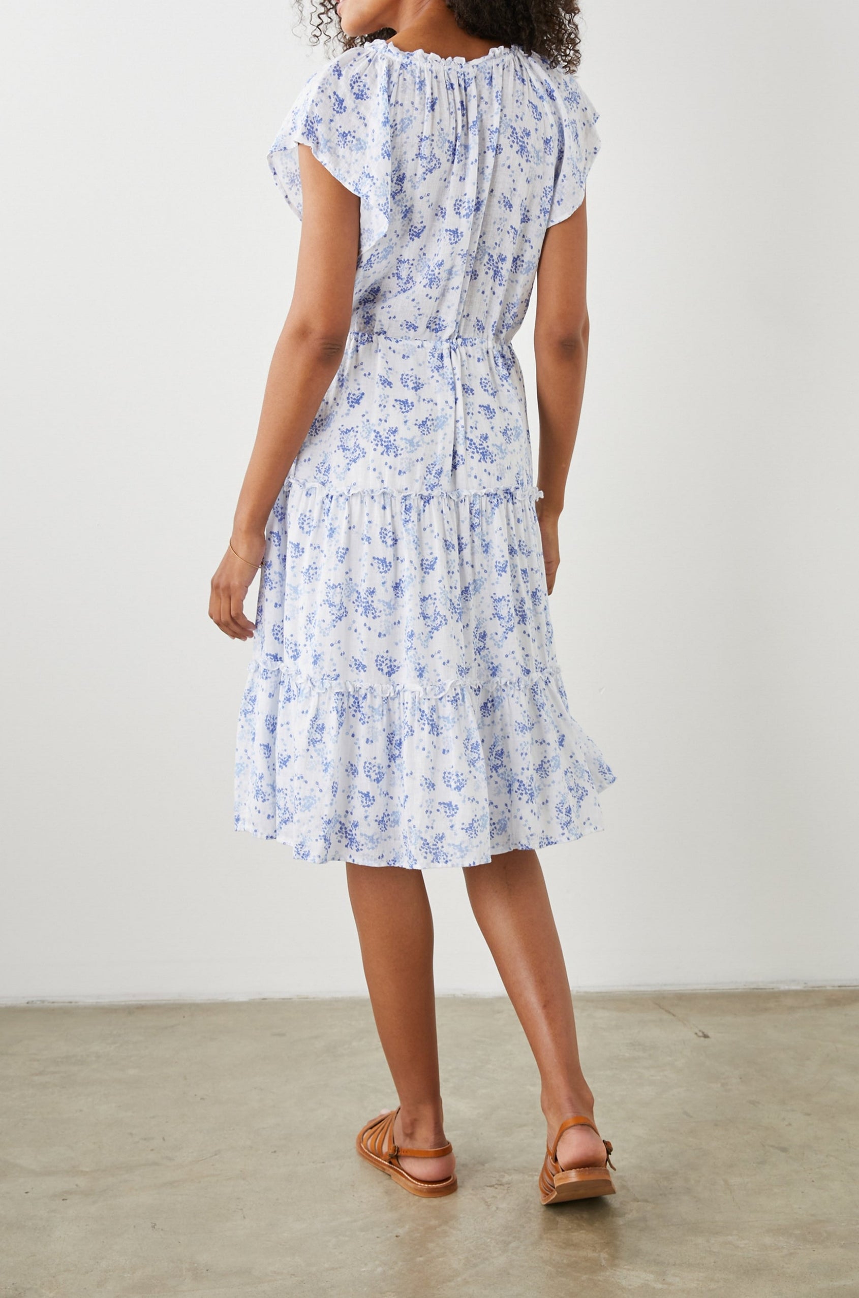 Juni Short Sleeve Midi Dress with a V Neck, Light Ruching along the Neckline, a Drawstring Waist, and a Tiered Skirt in Blue Blossoms Colorway, on White - Back Full Body View Featured on Model