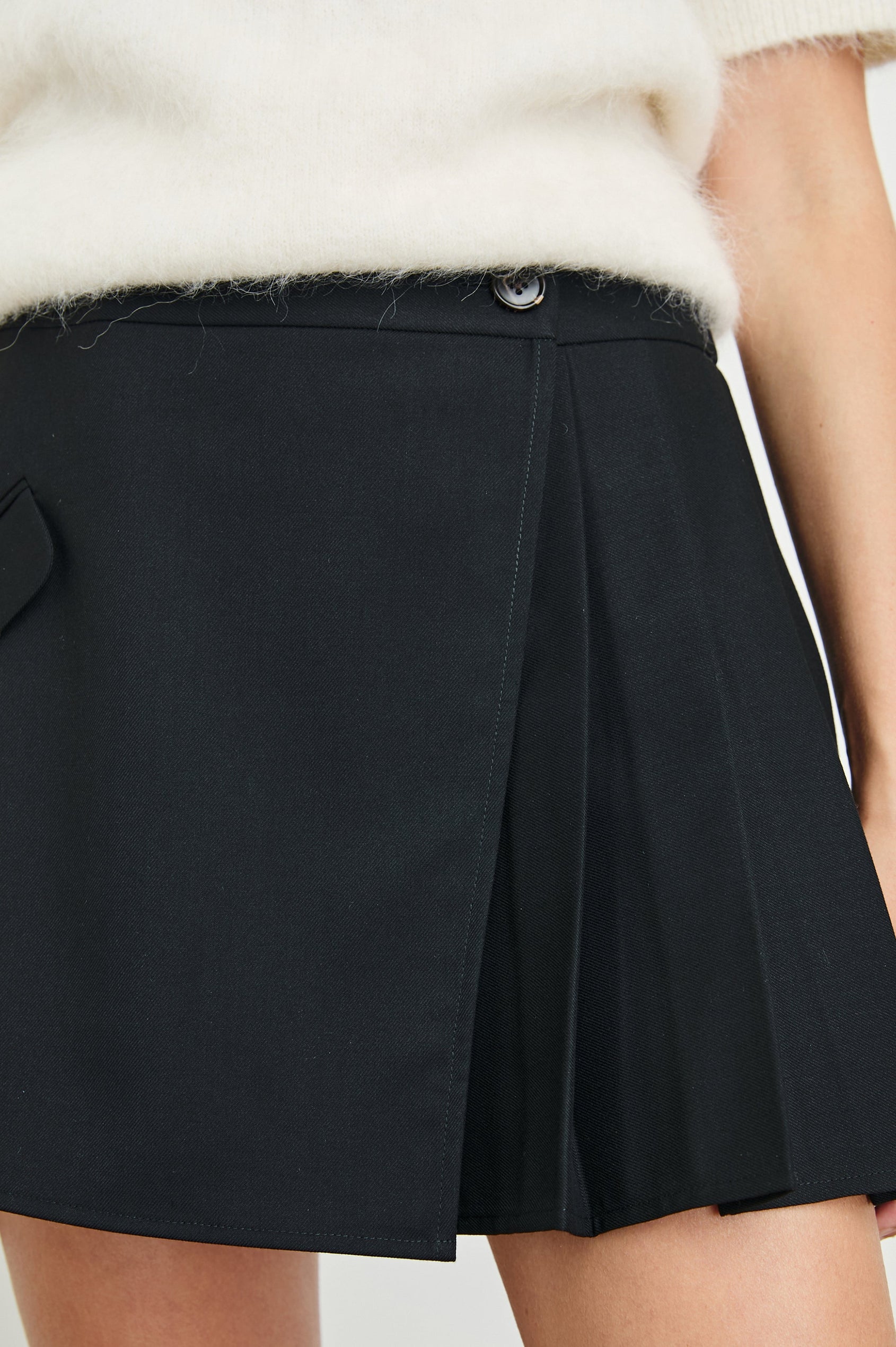 Adriana Mini Wrap Skirt with a Button, Front Flap Pocket and Pleats on Half the Skirt in Black Twill Colorway - Front View Featured on Model 