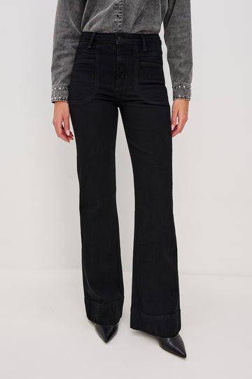 Alamitos is a high waisted denim trouser with flared leg and front patch pockets in Blackout colorway. Front view on model