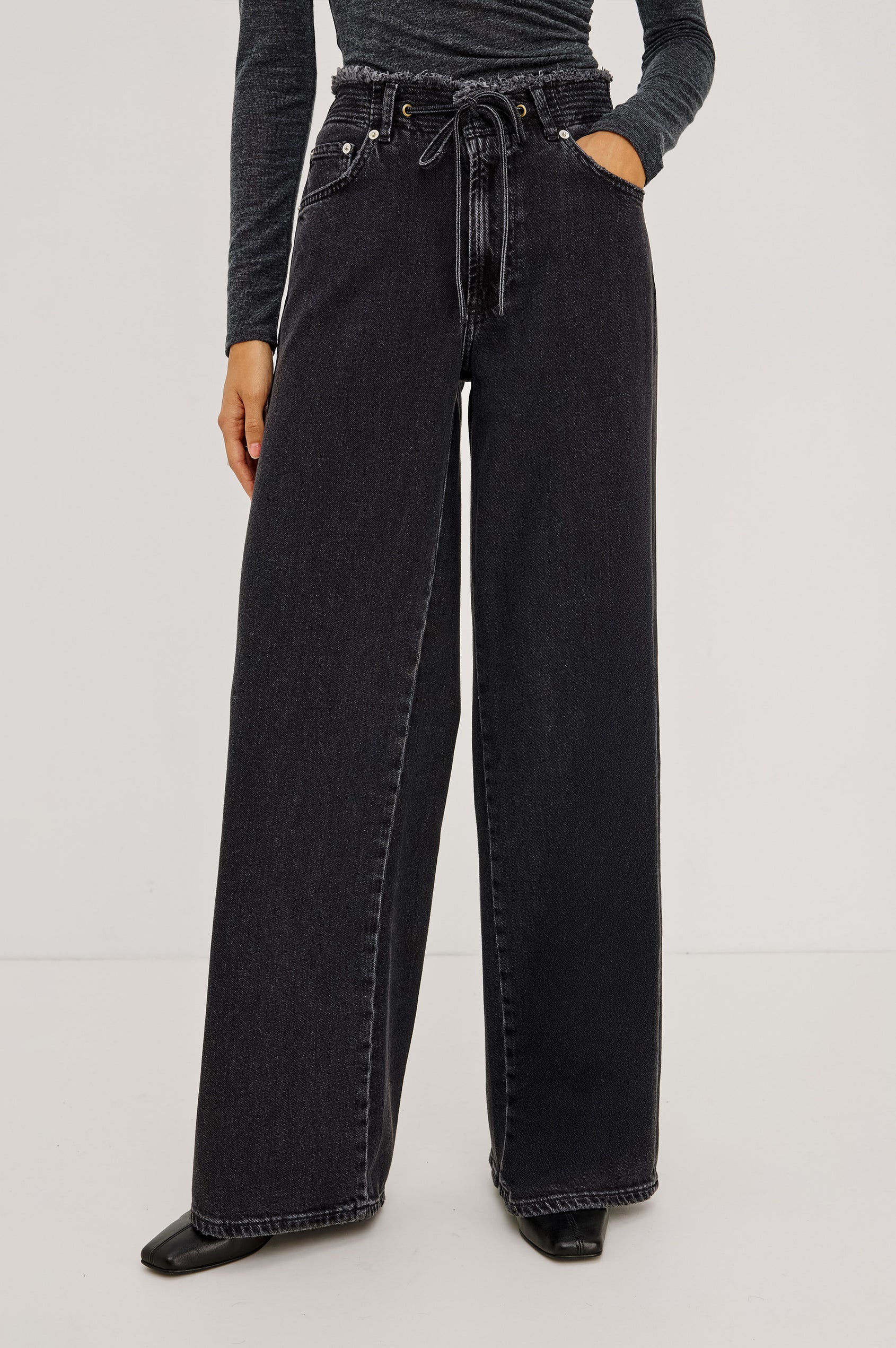Angeleno Wide Leg in Rigid Denim With Hidden Stretch, Relaxed Mid-Rise Fit, 5-Pockets, Self-Tie Shoelace Belt, and Frayed Waistband in Ash Black Colorway - Lower Body Front View Featured on Model
