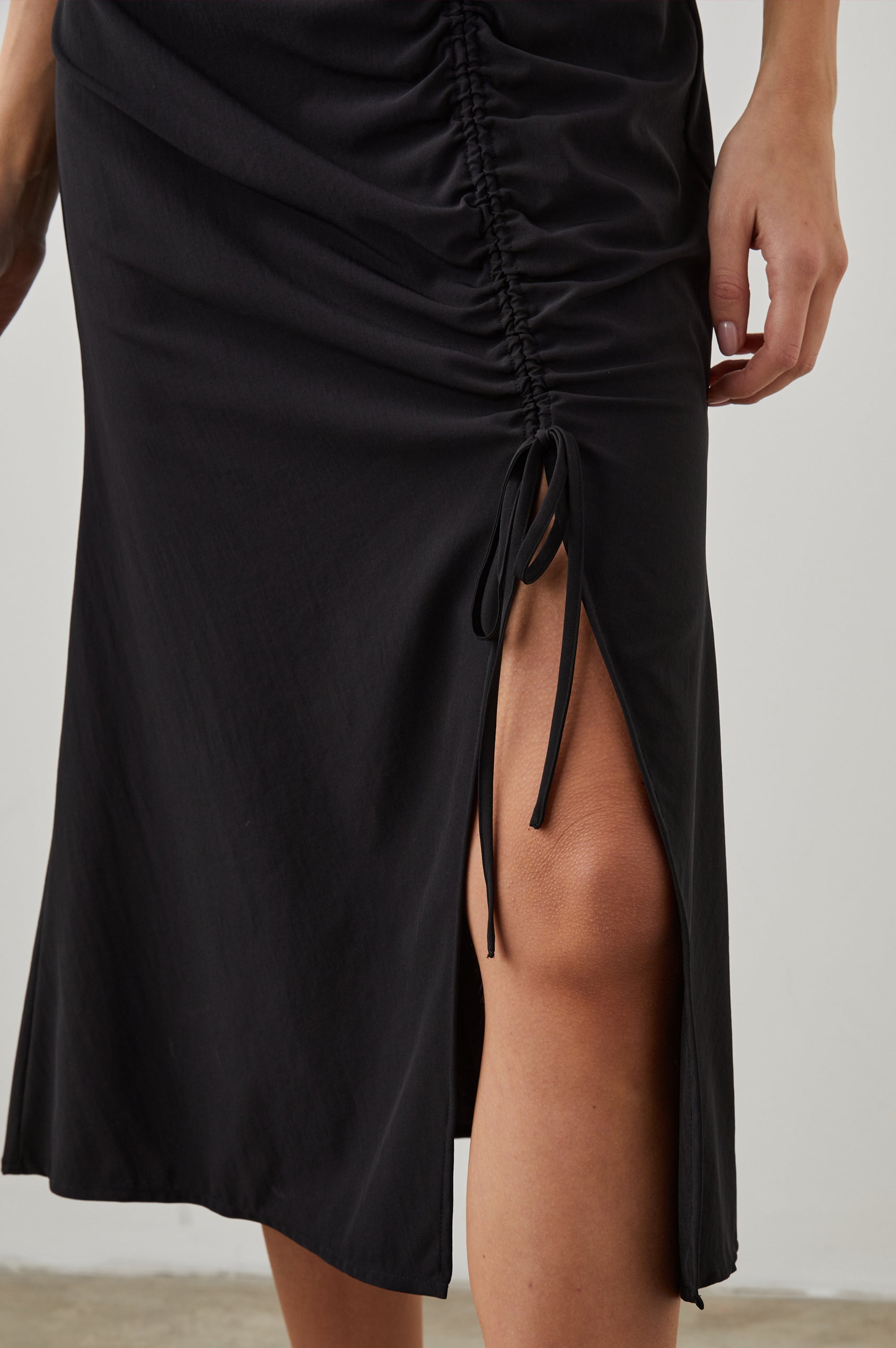 Auren Midi Dress with Cap Sleeves, a Deep V Neck, a Mid-Thigh Side Slit and Ruching from the V Neck to the Slit with a Drawcord at the Slit in Black Colorway - Front View Featured on Model 