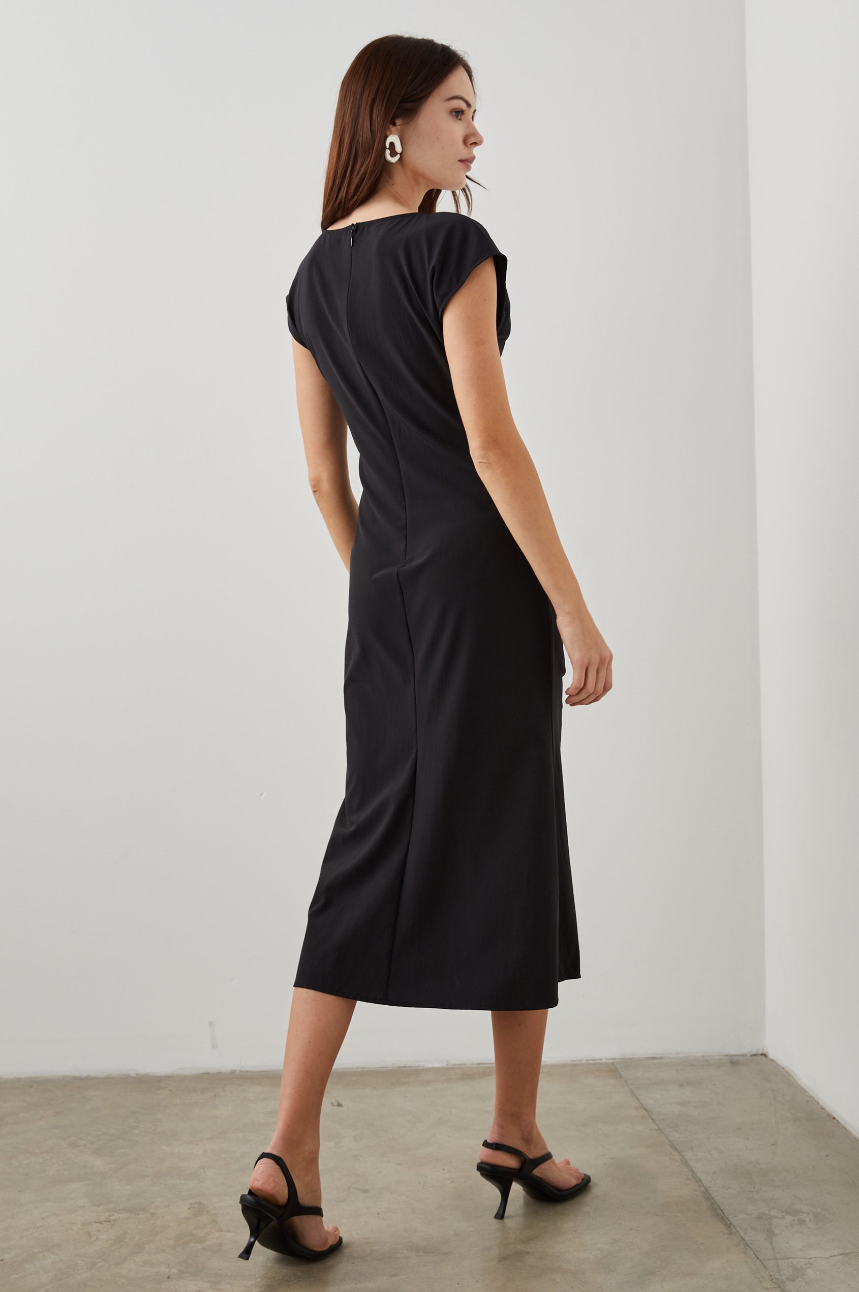 Auren Midi Dress with Cap Sleeves, a Deep V Neck, a Mid-Thigh Side Slit and Ruching from the V Neck to the Slit with a Drawcord at the Slit in Black Colorway - Back Full Body View Featured on Model 