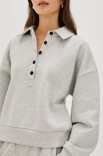 Cotton polo-style sweatshirt made from French terry fabric. The design features a button-front half placket, drop shoulders, and binding at the hem and cuffs for a relaxed, comfortable fit in Heather Grey Colorway - Close up view featured on model 
