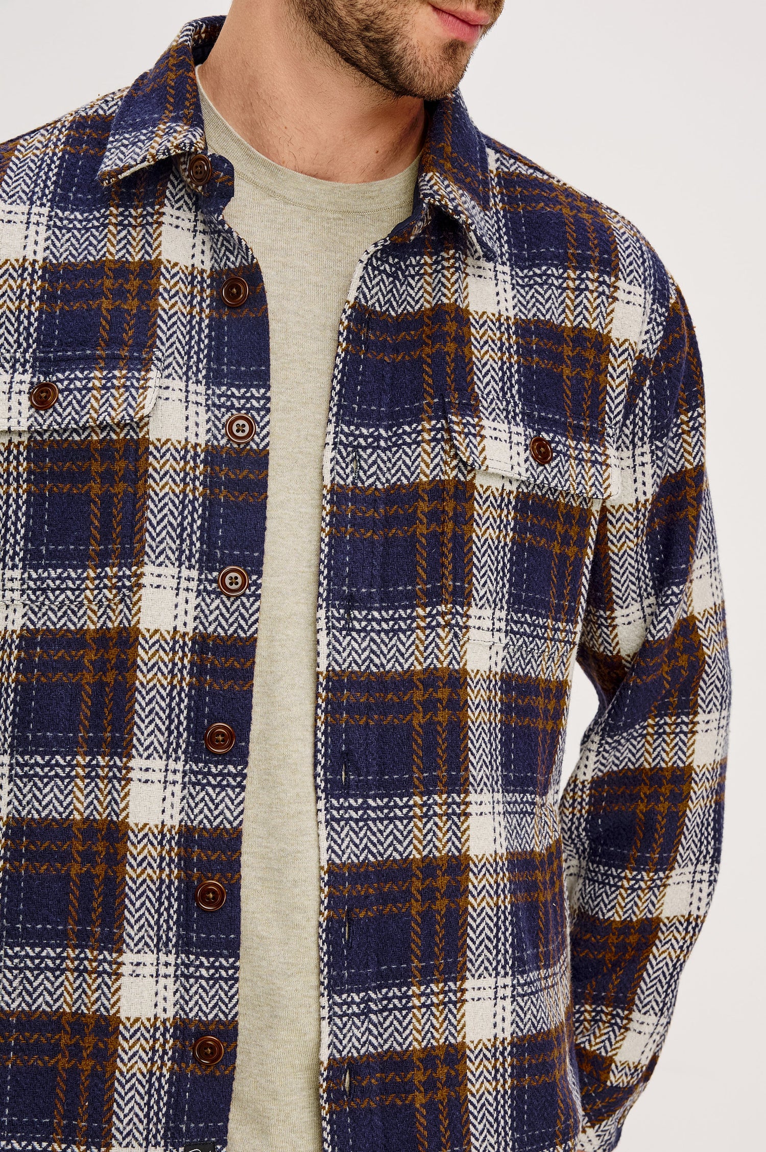 The Berkshire is a plaid shirt jacket with two chest pockets button front and collar in Navy Umber Cream colorway. Front detail view featured on model.