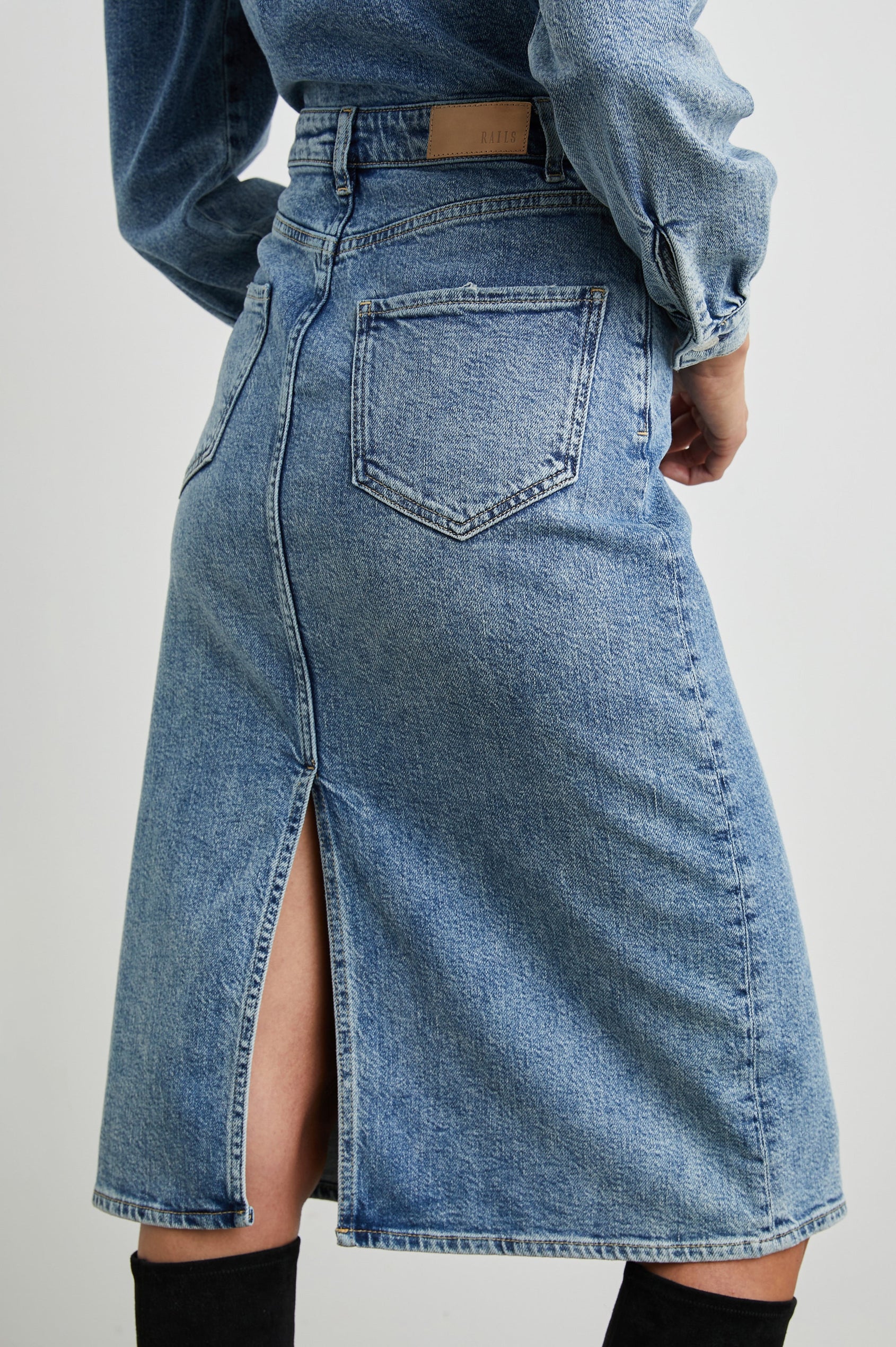 Beverly Long Sleeve Denim Knee Dress with a Back Vent, Belt Loops, a Button and Zipper Closure for the Skirt and Button Closure on the Bodice, a Collar, two Front Pockets plus a Coin Pocket and Two Back Patch Pockets in West Coast Colorway, a Blue - Back View Featured on Model