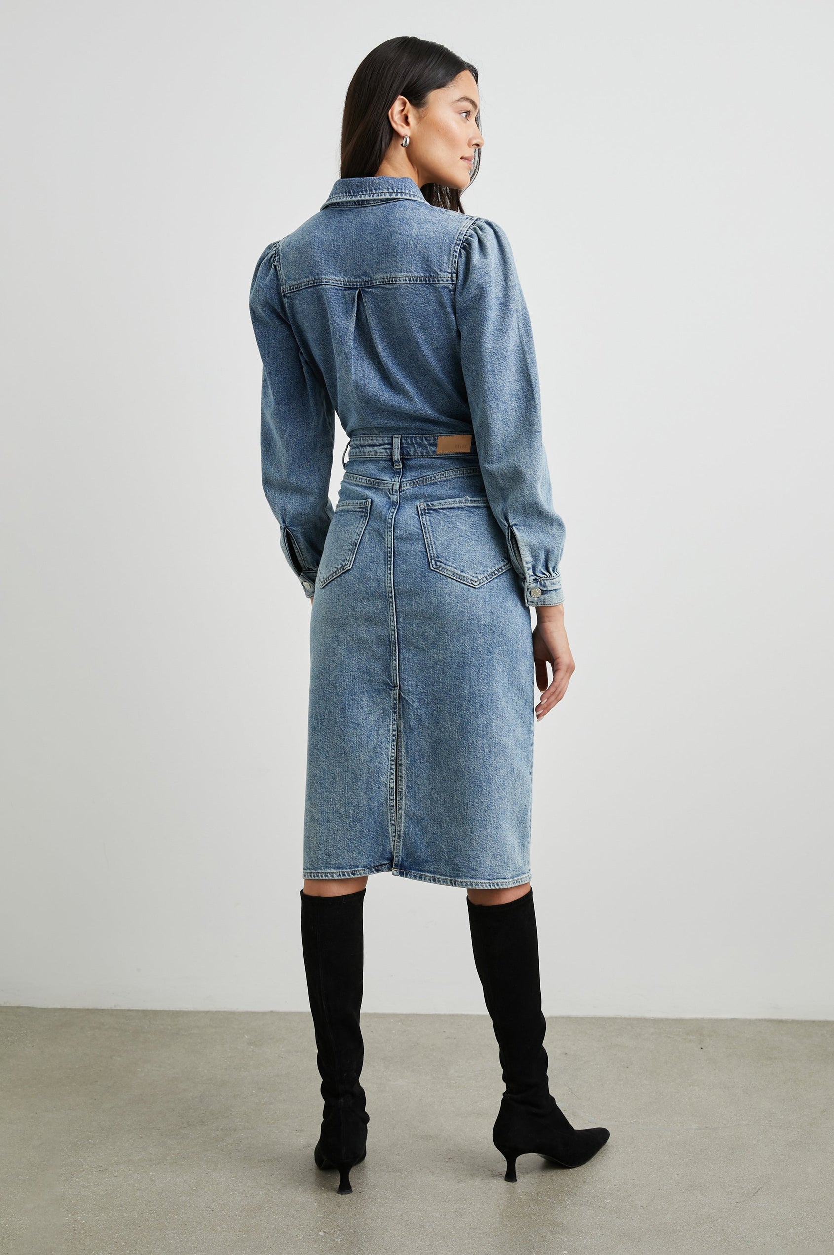 Beverly Long Sleeve Denim Knee Dress with a Back Vent, Belt Loops, a Button and Zipper Closure for the Skirt and Button Closure on the Bodice, a Collar, two Front Pockets plus a Coin Pocket and Two Back Patch Pockets in West Coast Colorway, a Blue - Back Full Body View Featured on Model