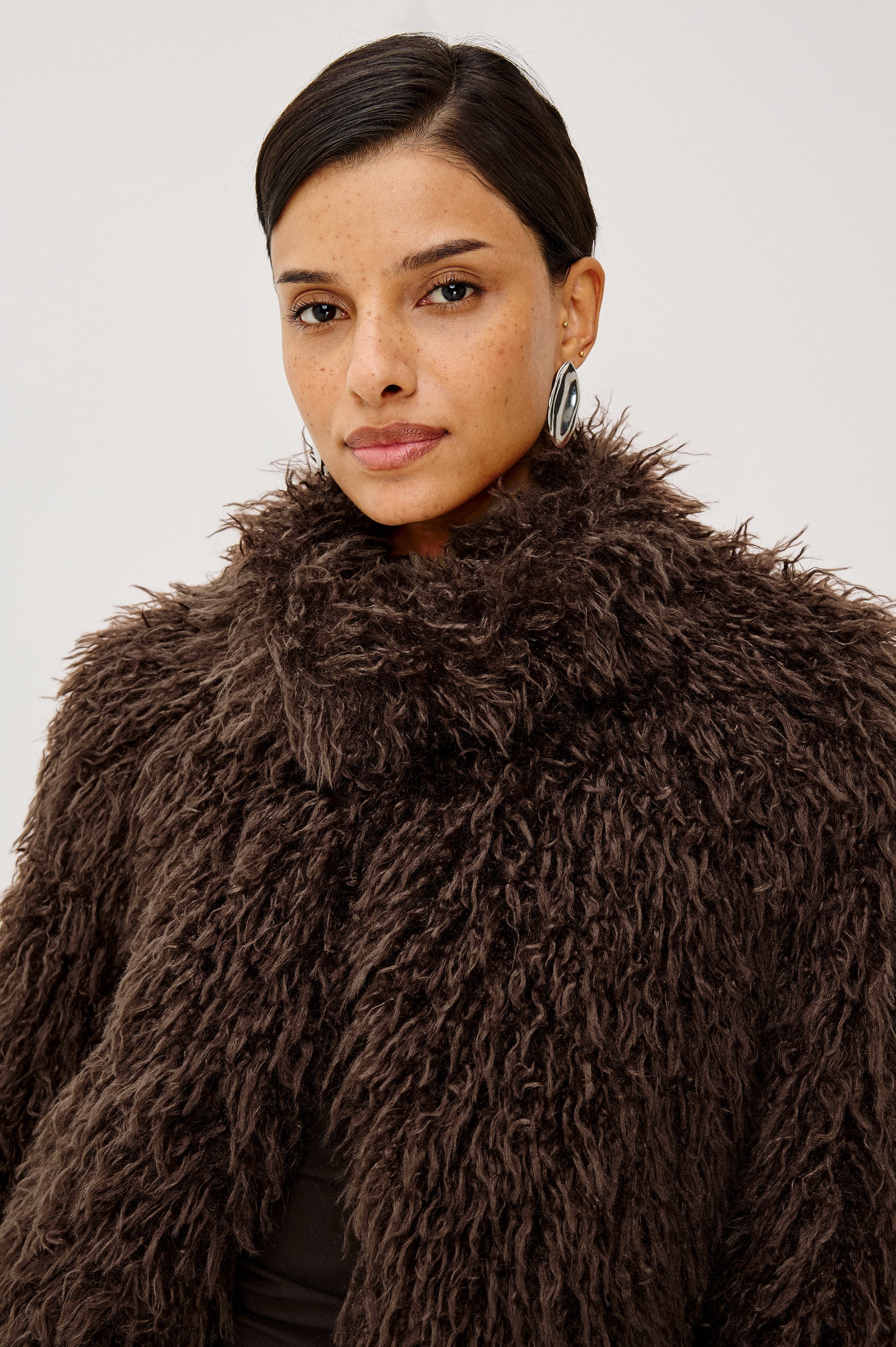 Blisse Jacket in Faux Mongolian Fur With Boxy Slightly Cropped Cropped Silhouette, Collar, Satin-Like Lining, Side Pocketts, and Front Hook-And-Eye Closure in Espresso Colorway - Upper Body Front View Featured on Model