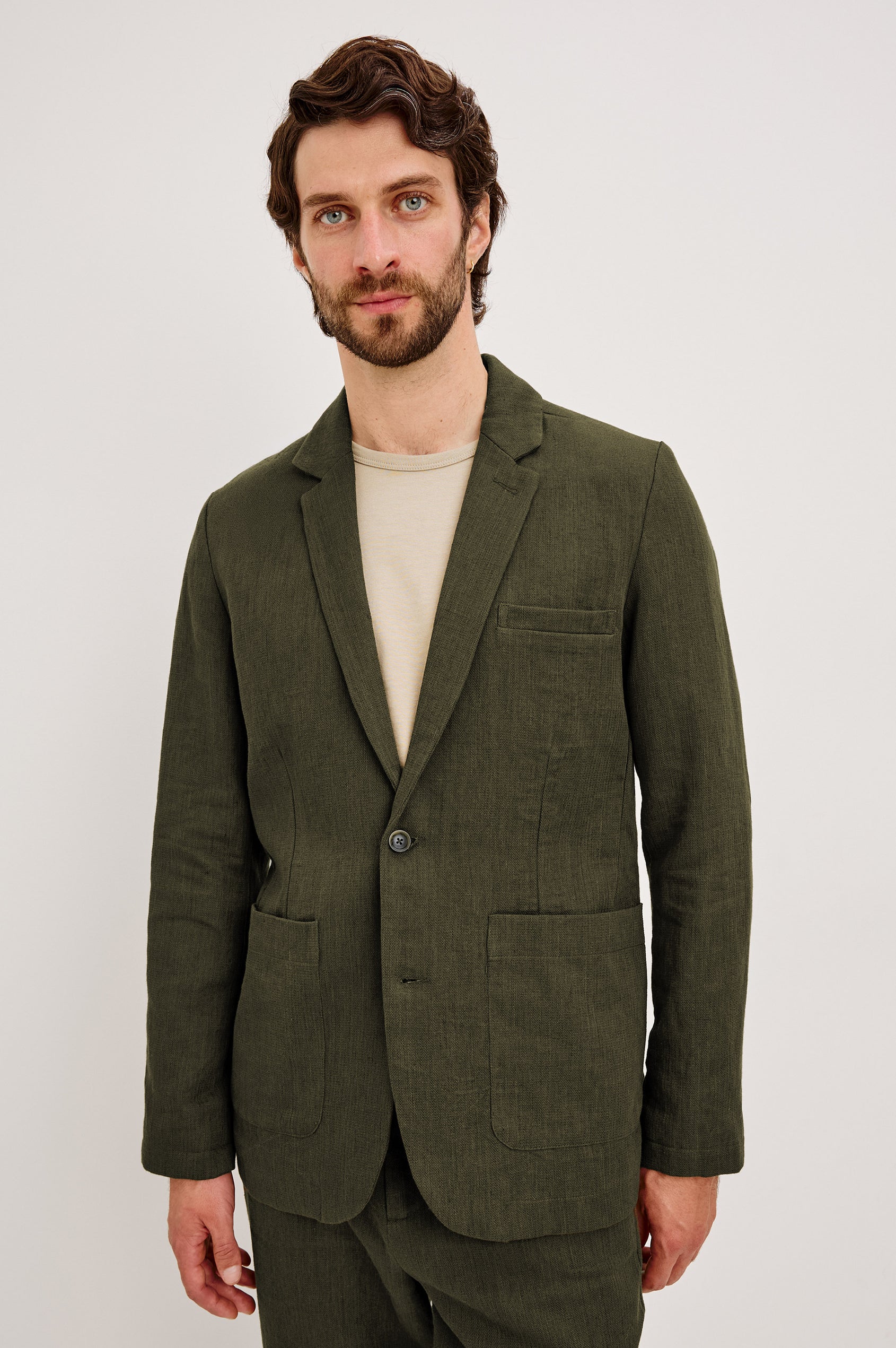 The Bond is a single breasted blazer with two buttons, one chest pocket and two patch pockets in Deep Olive colorway. Front view featured on model.