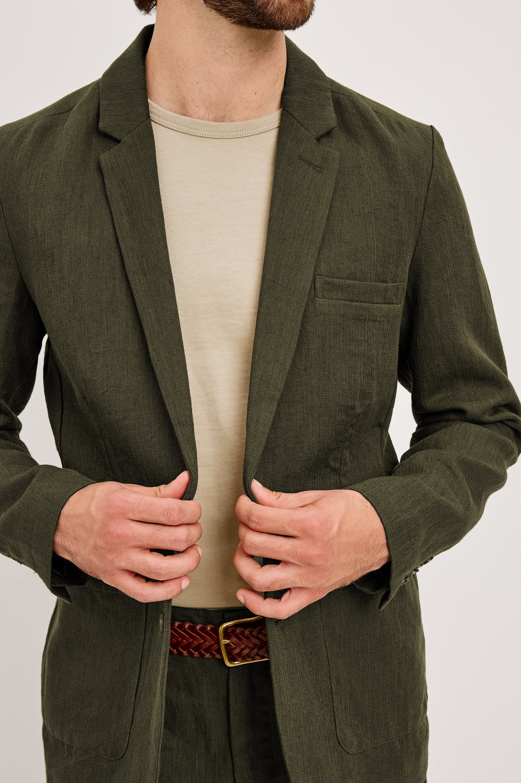 The Bond is a single breasted blazer with two buttons, one chest pocket and two patch pockets in Deep Olive colorway. Front detailed view featured on model.