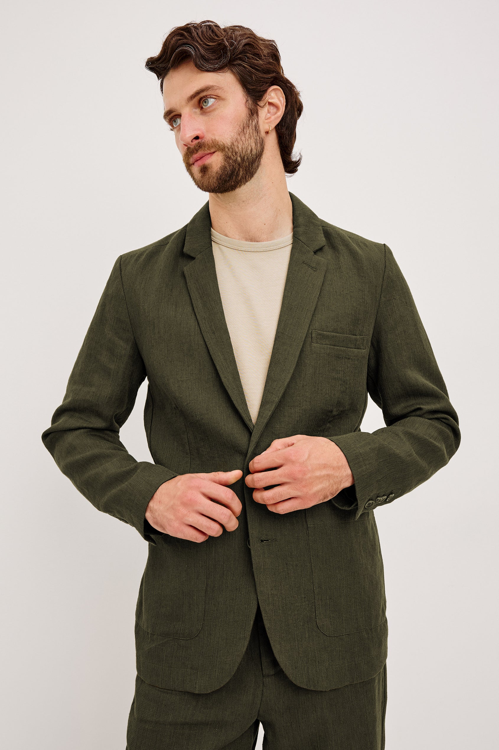 The Bond is a single breasted blazer with two buttons, one chest pocket and two patch pockets in Deep Olive colorway. Front view featured on model.