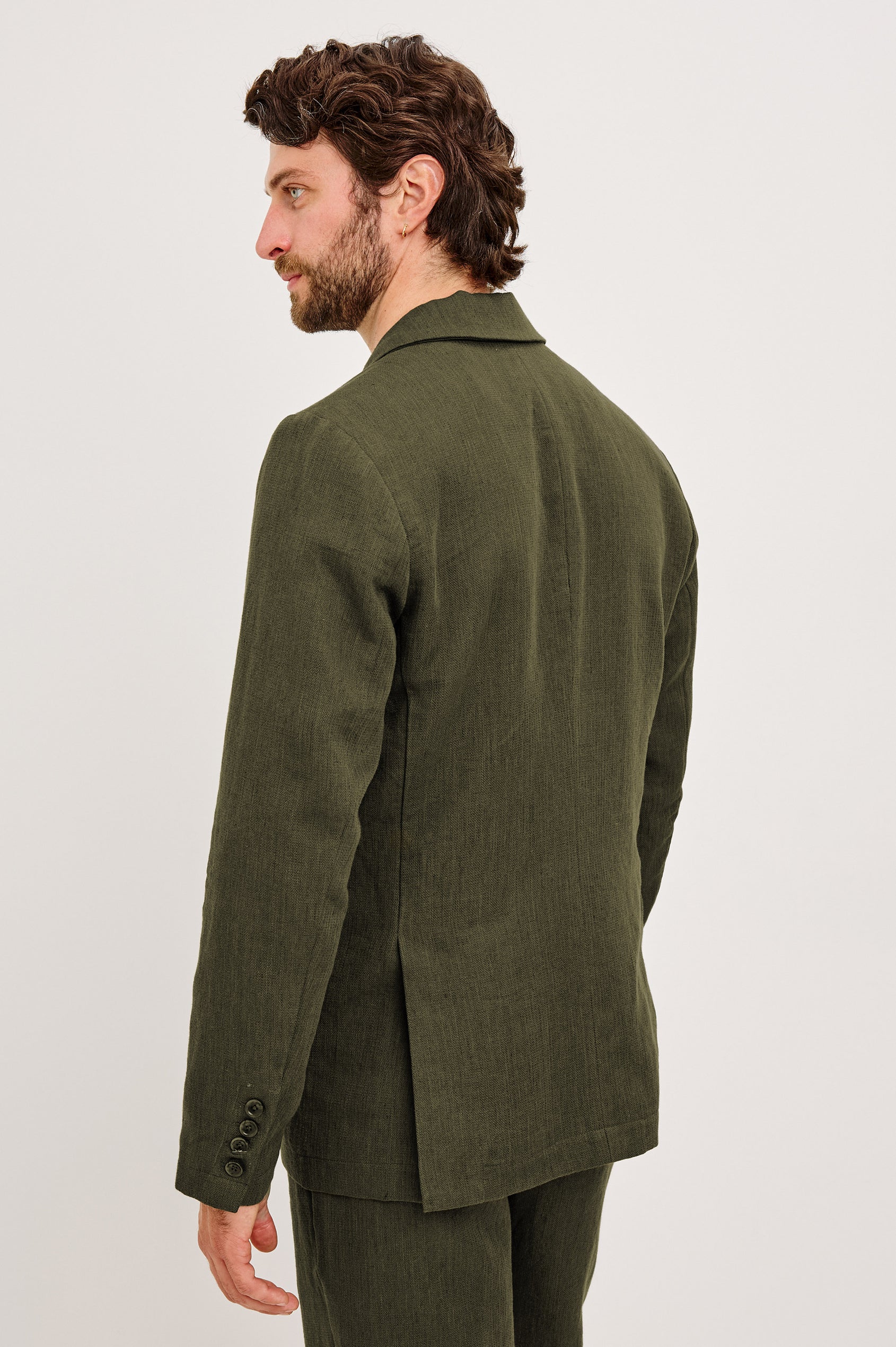 The Bond is a single breasted blazer with two buttons, one chest pocket and two patch pockets in Deep Olive colorway. Back view featured on model.
