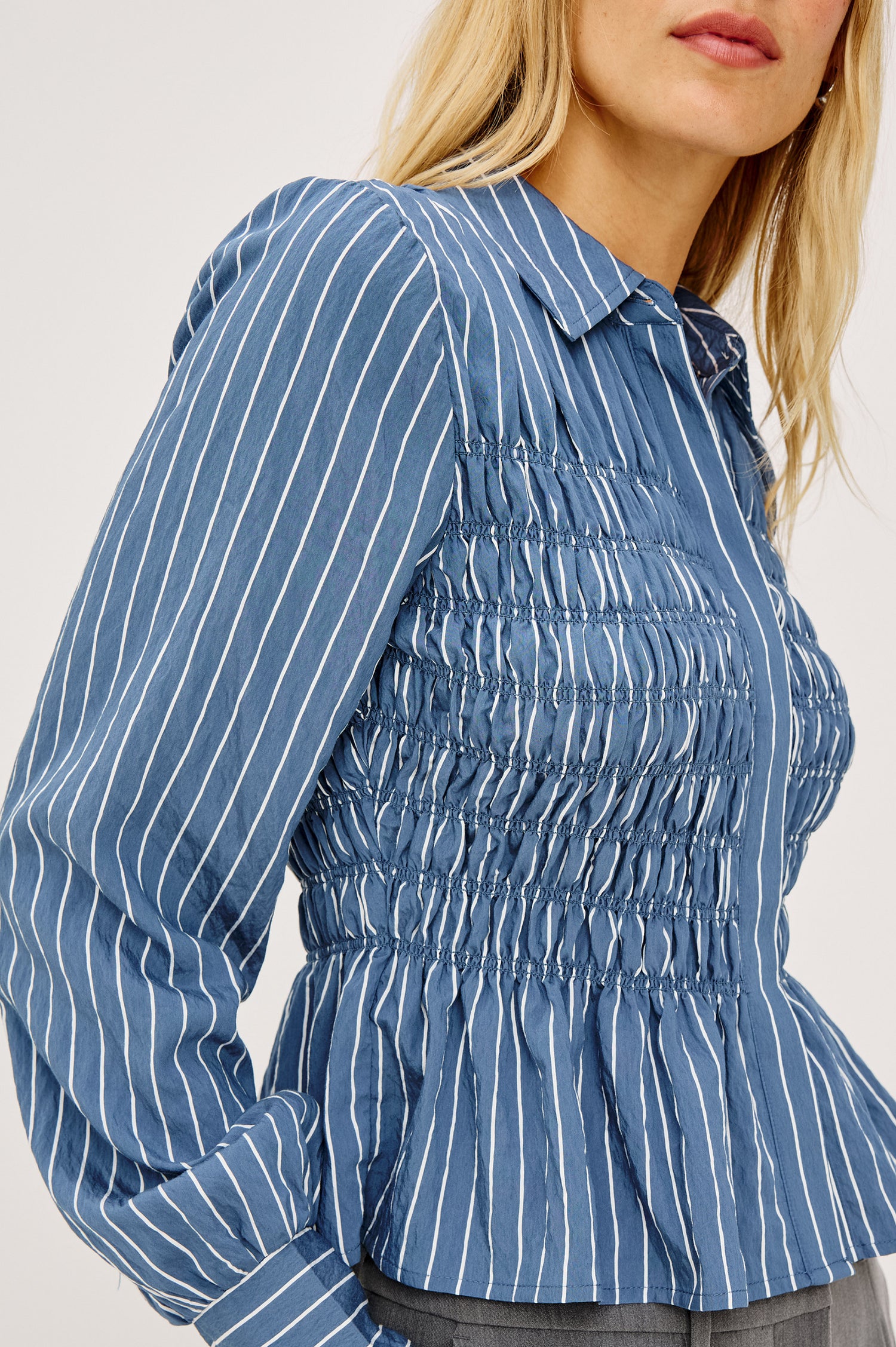 Bradshaw Shirt in Cotton Poplin With Button-Up Front, Collar, Smocked Body, Peplum Hem, and Bishop Sleeves in Washed Indigo Stripe Colorway - Upper Body Side View Featured on Model