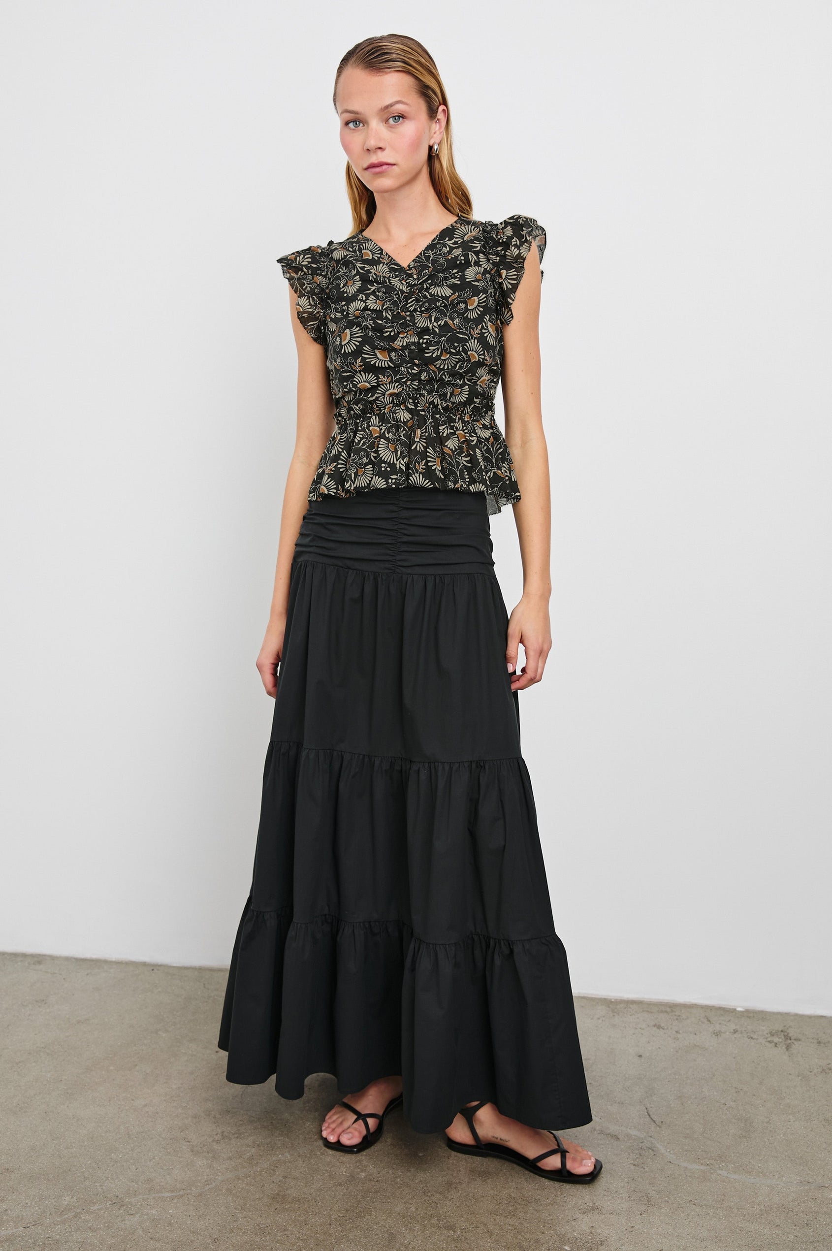 Cali Top with Flutter Sleeves, a V Neckline, Horizontal pleats along the bodice and vertical pleats at the hem in Cassia Colorway, with white and orange flowers on black - Front Full Body View Featured on Model