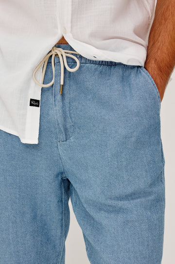 Callum Tapered Straight Leg Pant in Linen Twill With Adjustable Drawstring Waistband Ties in Medium Wash Indigo Colorway - Lower Body Front View Featured on Model