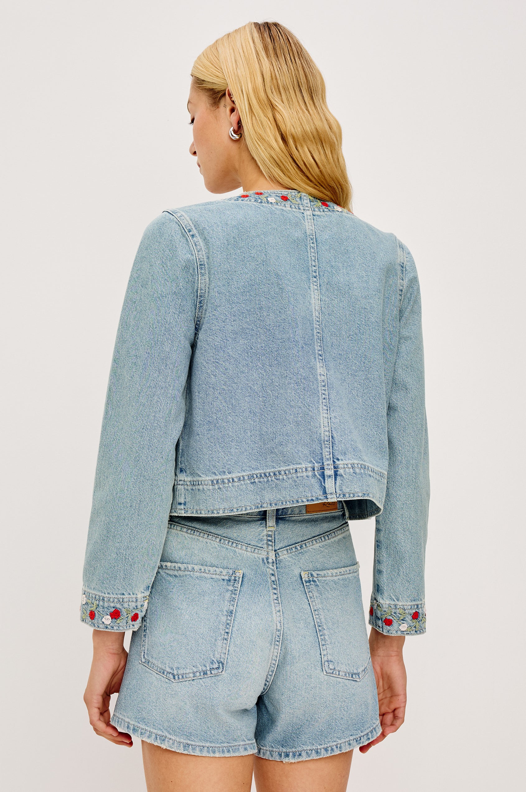 The Capistrano is a cropped denim jacket with a scoop neck, a button front, two chest pockets in Floral laser colorway. Back view featured on model.