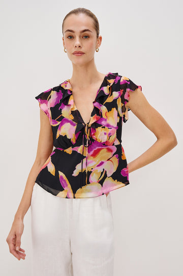 Carmine blouse, a chiffon top with ruffled cap sleeves, ruffles at the v-neckline, a front tie, and empire waist silhouette in Dusk Orchid Colorway. Front View Shown on Model.