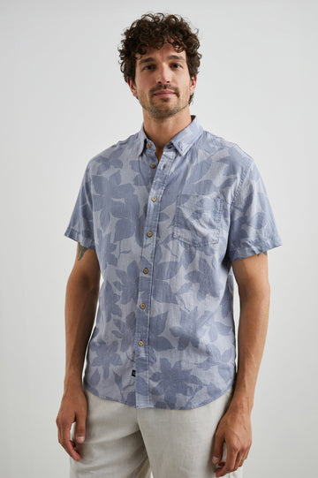 Carson Short Sleeve Button Up with a Chest Patch Pocket in Garden Sands Orchid Colorway, Blue Flowers on Light Blue - Front View Featured on Model