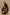 Caterine Maxi Dress with Mid-length Sleeves, a V neck, a Shirred Collar with a tie, a Smocked Waist, and a Tiered Skirt in Brown Nala Colorway - Stylized Front View of Model Squatting