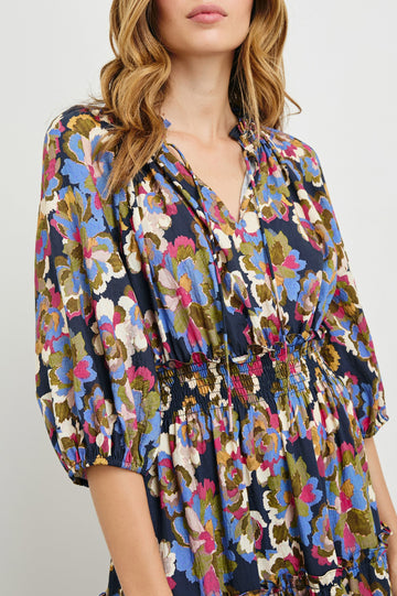 Caterine Maxi Dress with Mid-length Sleeves, a V neck, a Shirred Collar with a tie, a Smocked Waist, and a Tiered Skirt in Navy Wildflower Colorway, flowers in creams, pinks, greens and blues on Navy - Front View Featured on Model