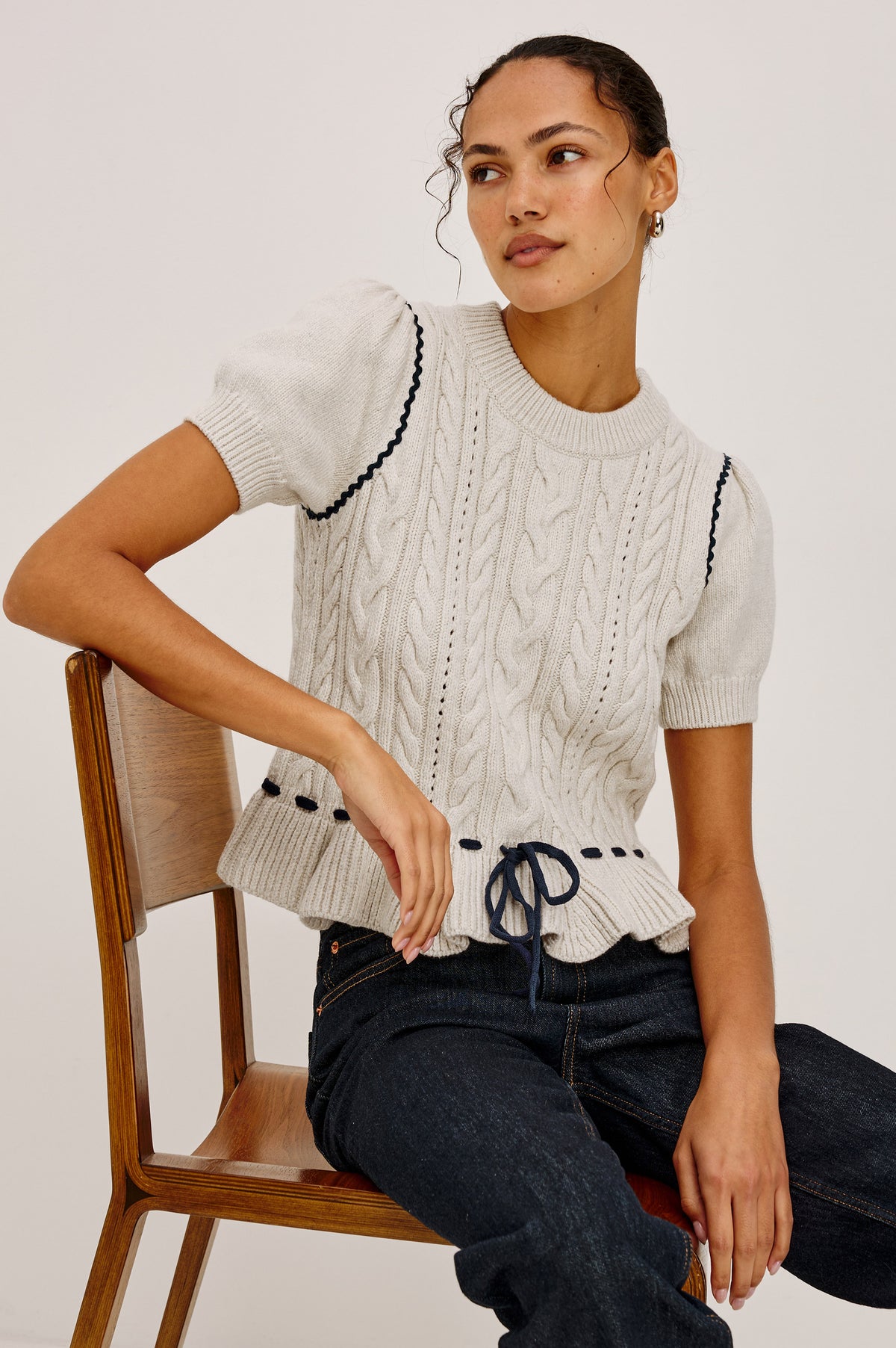 Chandi Sweater in Cable Knit With Short Puff Sleeves, Fitted SIlhouette, Soft Flared Peplum Hem, and Contrast Serpentine Trim and Interlocking Drawstring Ties in Heather Oat Colorway - Upper Body Front View Featured on Model