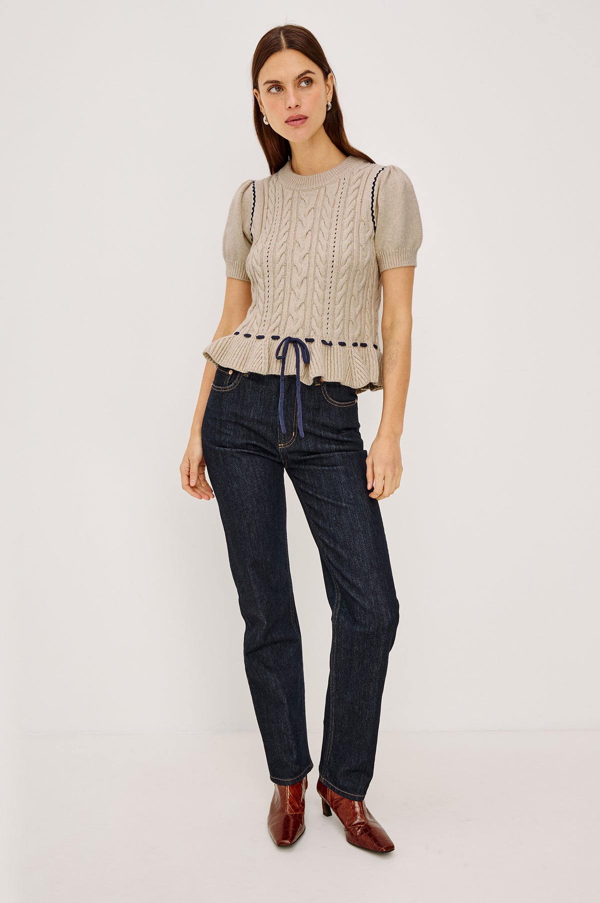 Chandi Sweater in Cable Knit With Short Puff Sleeves, Fitted SIlhouette, Soft Flared Peplum Hem, and Contrast Serpentine Trim and Interlocking Drawstring Ties in Heather Oat Colorway - Full Body Front View Featured on Model