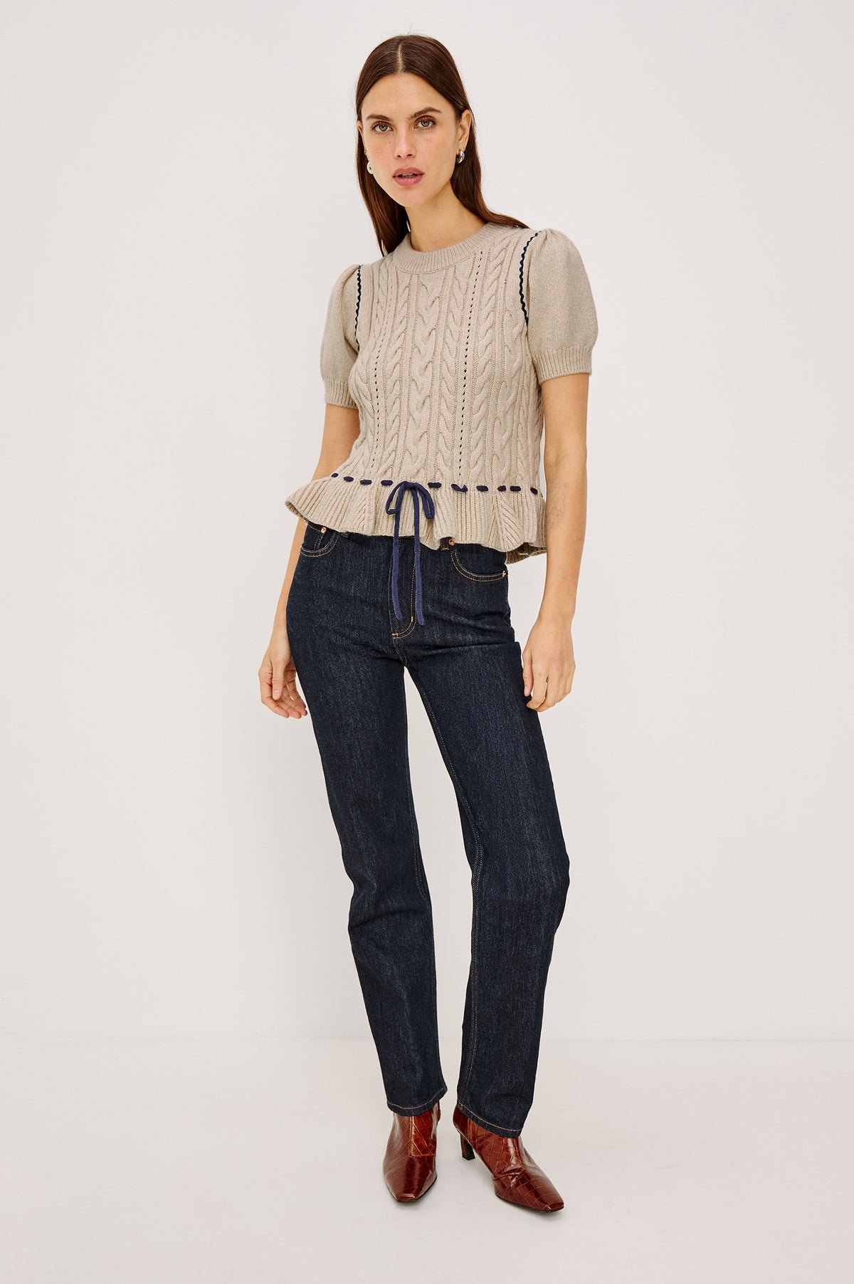 Chandi Sweater in Cable Knit With Short Puff Sleeves, Fitted SIlhouette, Soft Flared Peplum Hem, and Contrast Serpentine Trim and Interlocking Drawstring Ties in Heather Oat Colorway - Full Body Front View Featured on Model