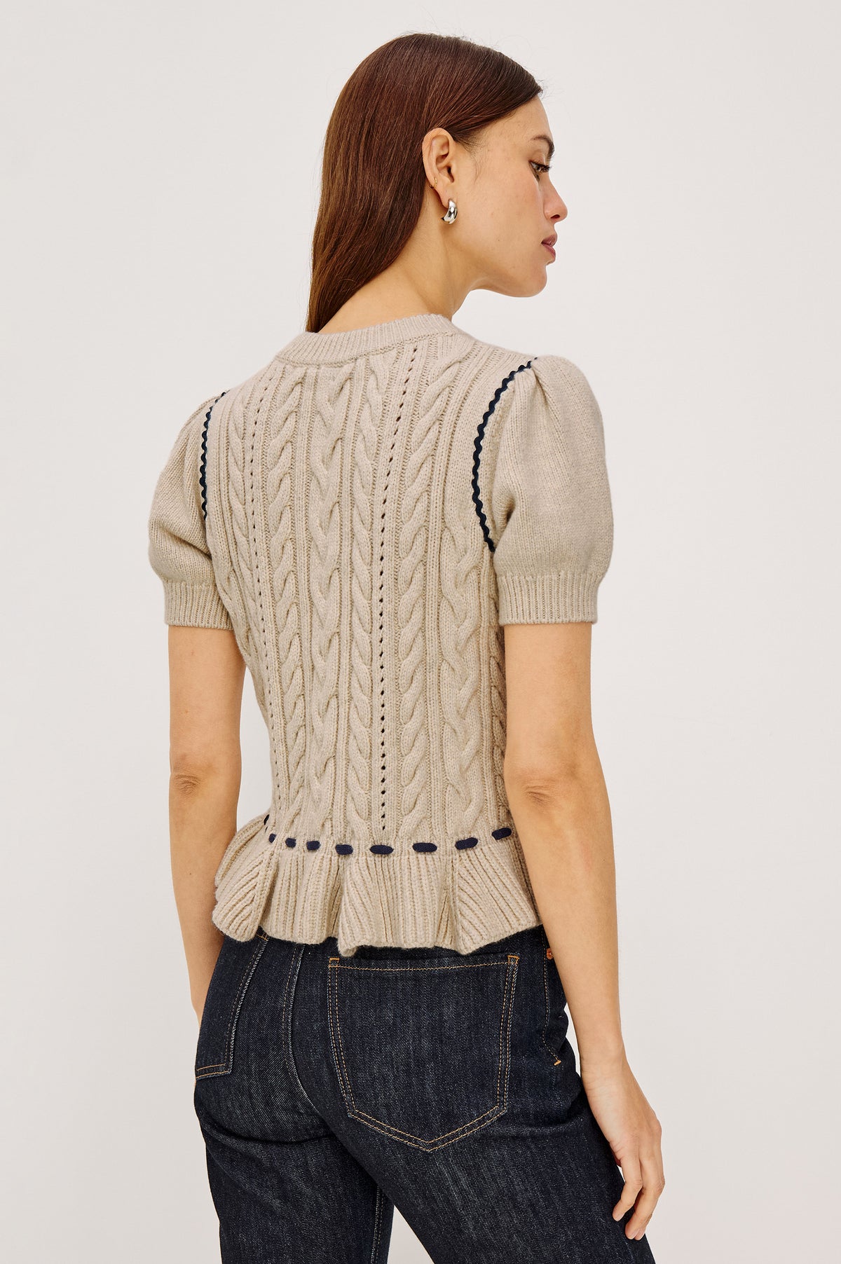 Chandi Sweater in Cable Knit With Short Puff Sleeves, Fitted SIlhouette, Soft Flared Peplum Hem, and Contrast Serpentine Trim and Interlocking Drawstring Ties in Heather Oat Colorway - Upper Body Back View Featured on Model