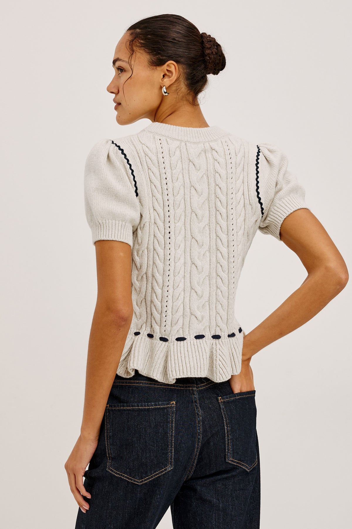 Chandi Sweater in Cable Knit With Short Puff Sleeves, Fitted SIlhouette, Soft Flared Peplum Hem, and Contrast Serpentine Trim and Interlocking Drawstring Ties in Heather Oat Colorway - Upper Body Back View Featured on Model