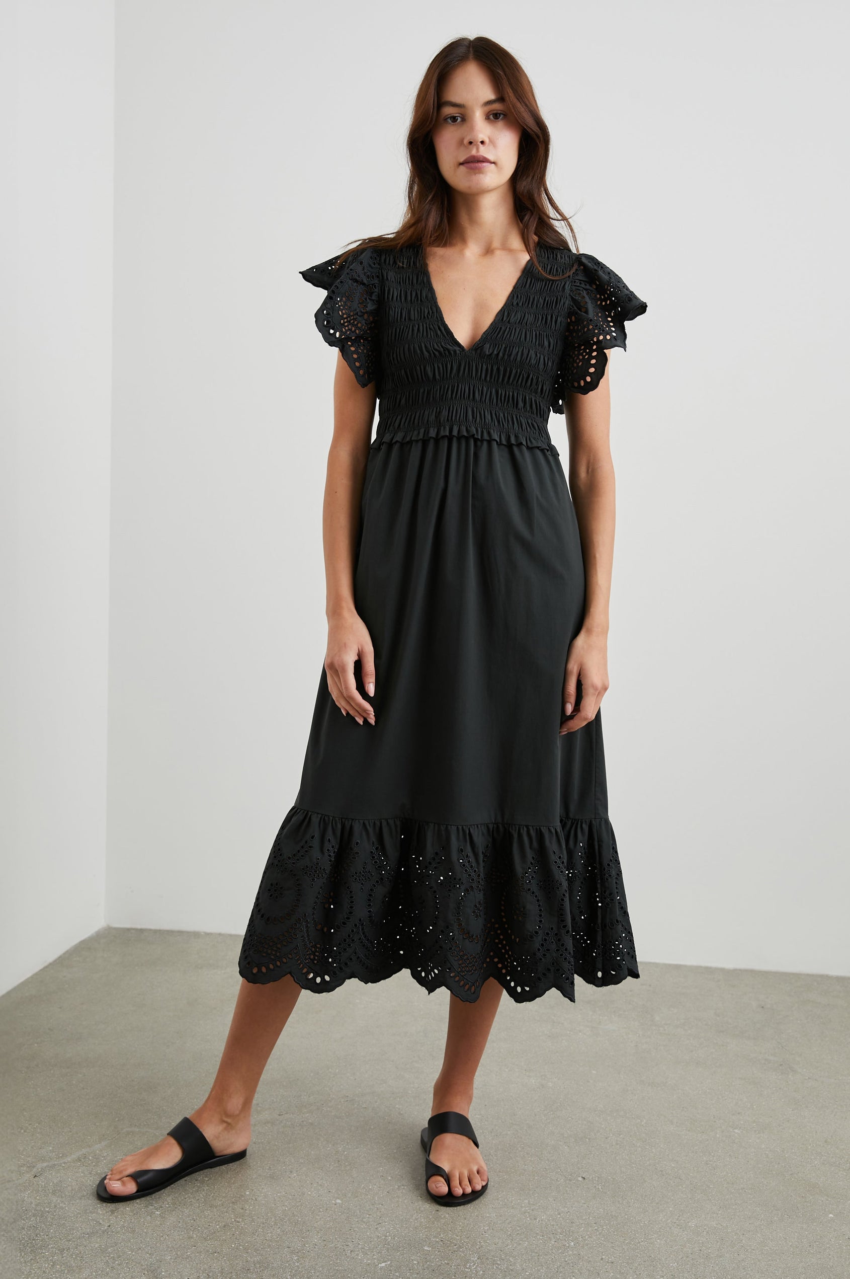 Clementine Midi Dress with a Deep V Neckline, Flutter Sleeves, Smocked Top, Two Side Pockets and eyelets on the Sleeves and Hem in Black Eyelet Colorway- Front Full Body View Featured on Model
