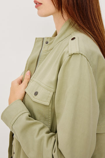 Collins Miitary Inspired Jacket With Shoulder Epaluettes Stand Collar Front Snap Buttons Double Chest Pockets Long Sleeves in Vintage Sage Colorway - Side Upper Body Close Up View Featured on Model