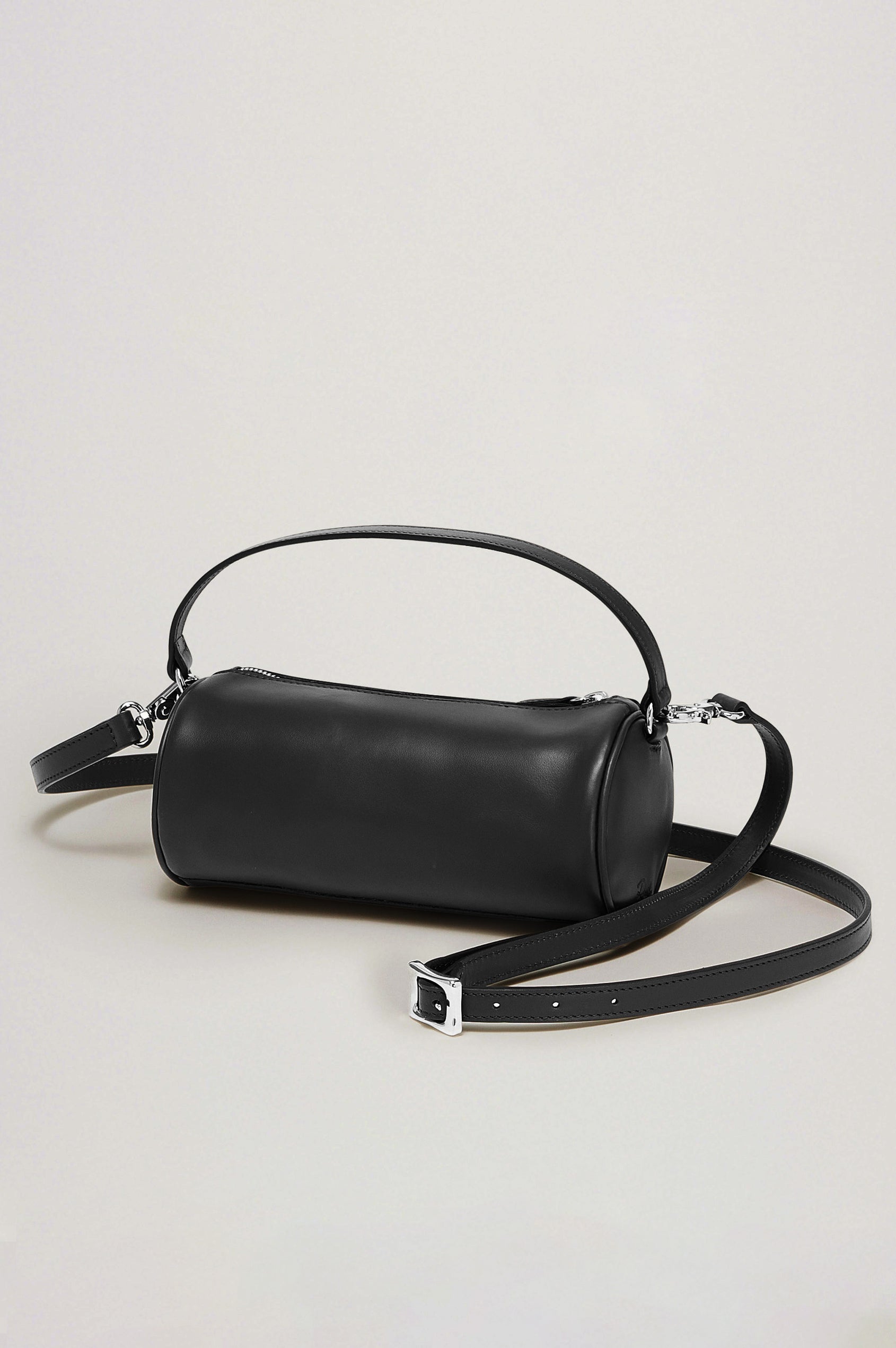 The Como is a mini barrel bag, made from smooth leather with a fixed top strap, a removable and adjustable buckled crossbody strap, a top zip, a side-embossed logo, and a branded interior label, in Black Leather colorway. Front view featured.