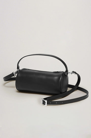 The Como is a mini barrel bag, made from smooth leather with a fixed top strap, a removable and adjustable buckled crossbody strap, a top zip, a side-embossed logo, and a branded interior label, in Black Leather colorway. Front view featured.
