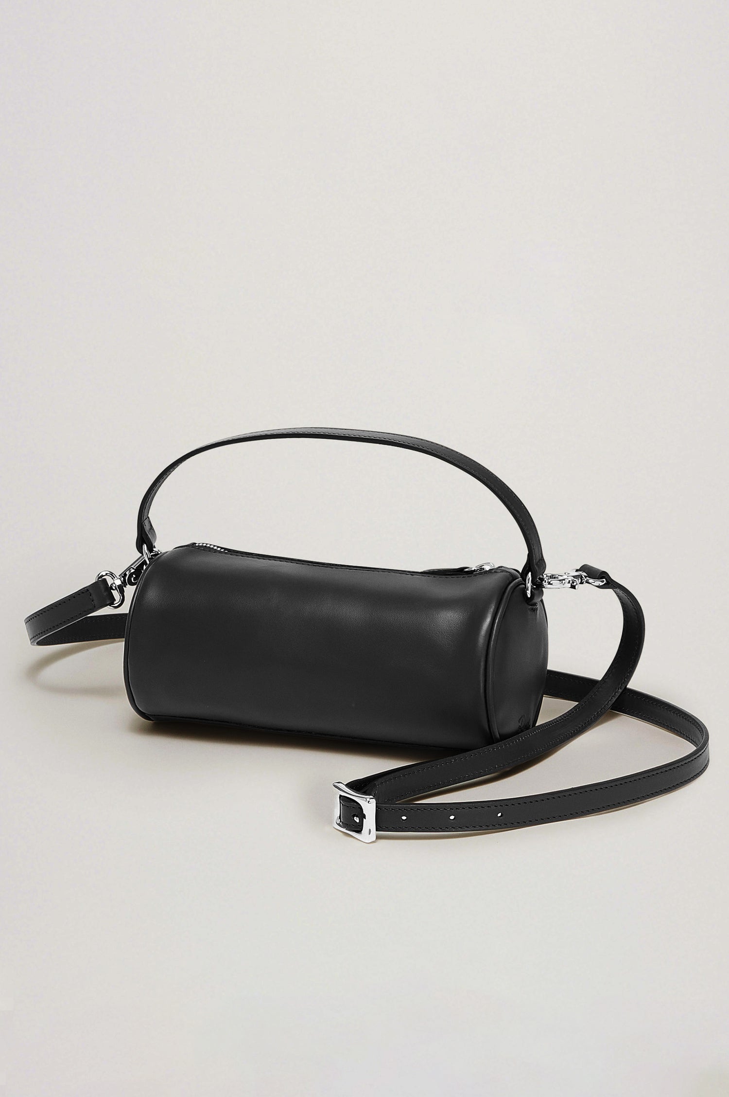 The Como is a mini barrel bag, made from smooth leather with a fixed top strap, a removable and adjustable buckled crossbody strap, a top zip, a side-embossed logo, and a branded interior label, in Black Leather colorway. Front view featured.